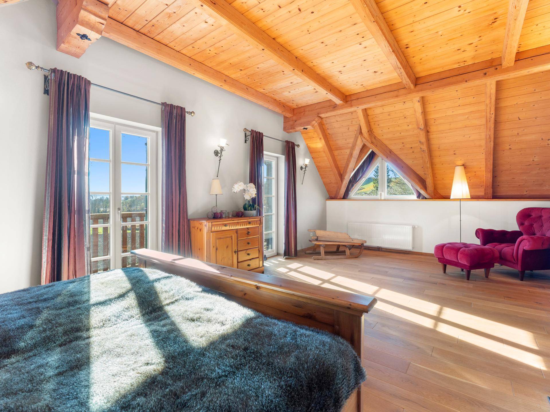 Helles Schlafzimmer mit Holzbalkendecke, Parkettboden und Zugang zu einem kleinen Balkon.