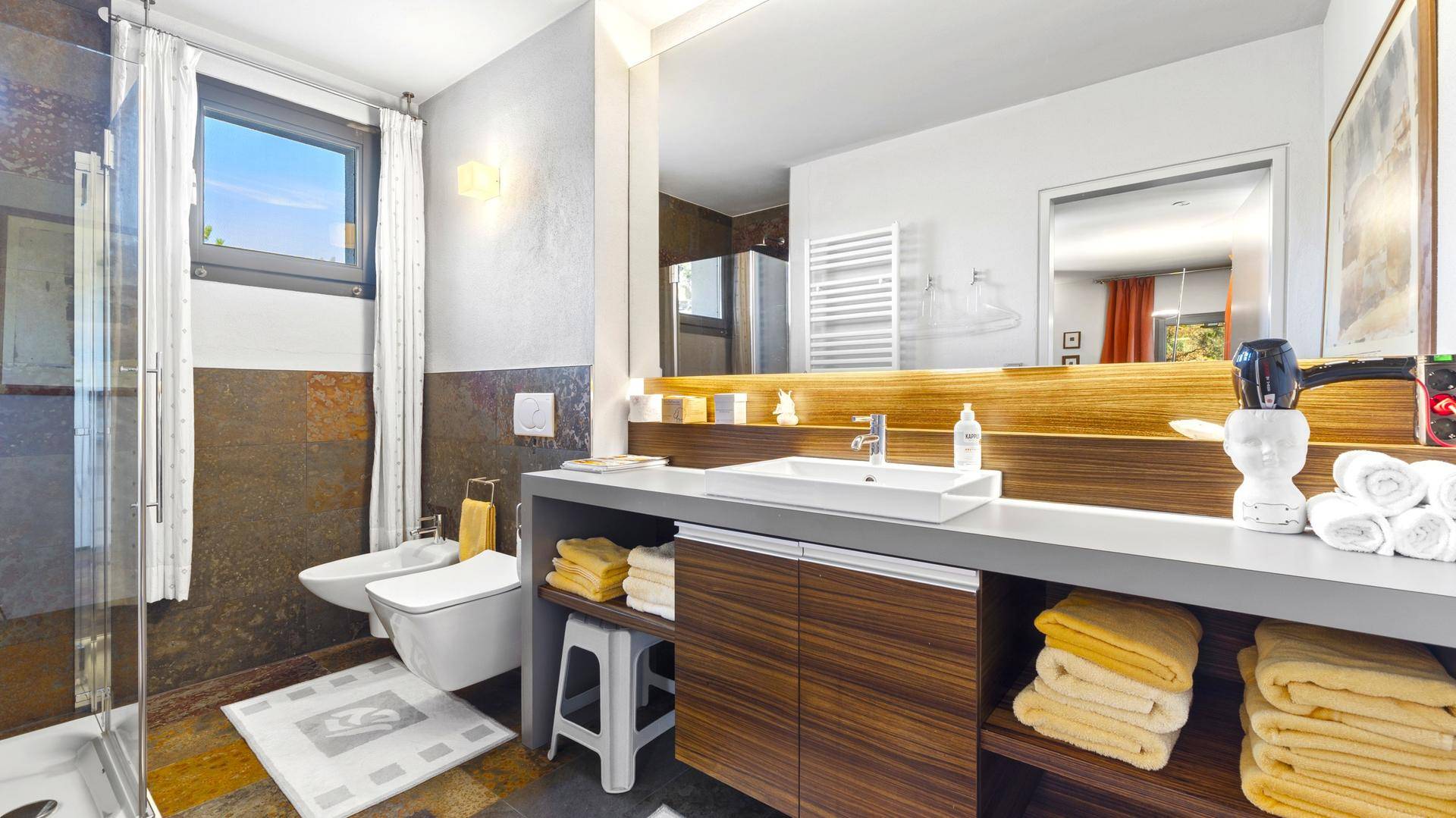 Modernes Badezimmer mit Dusche, Bidet, Einzelwaschbecken und Fenster für Tageslicht.