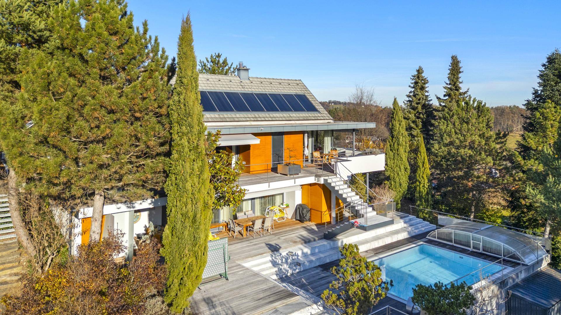 Panoramablick auf das moderne Haus mit Solaranlage, großem Poolbereich und üppiger Vegetation.