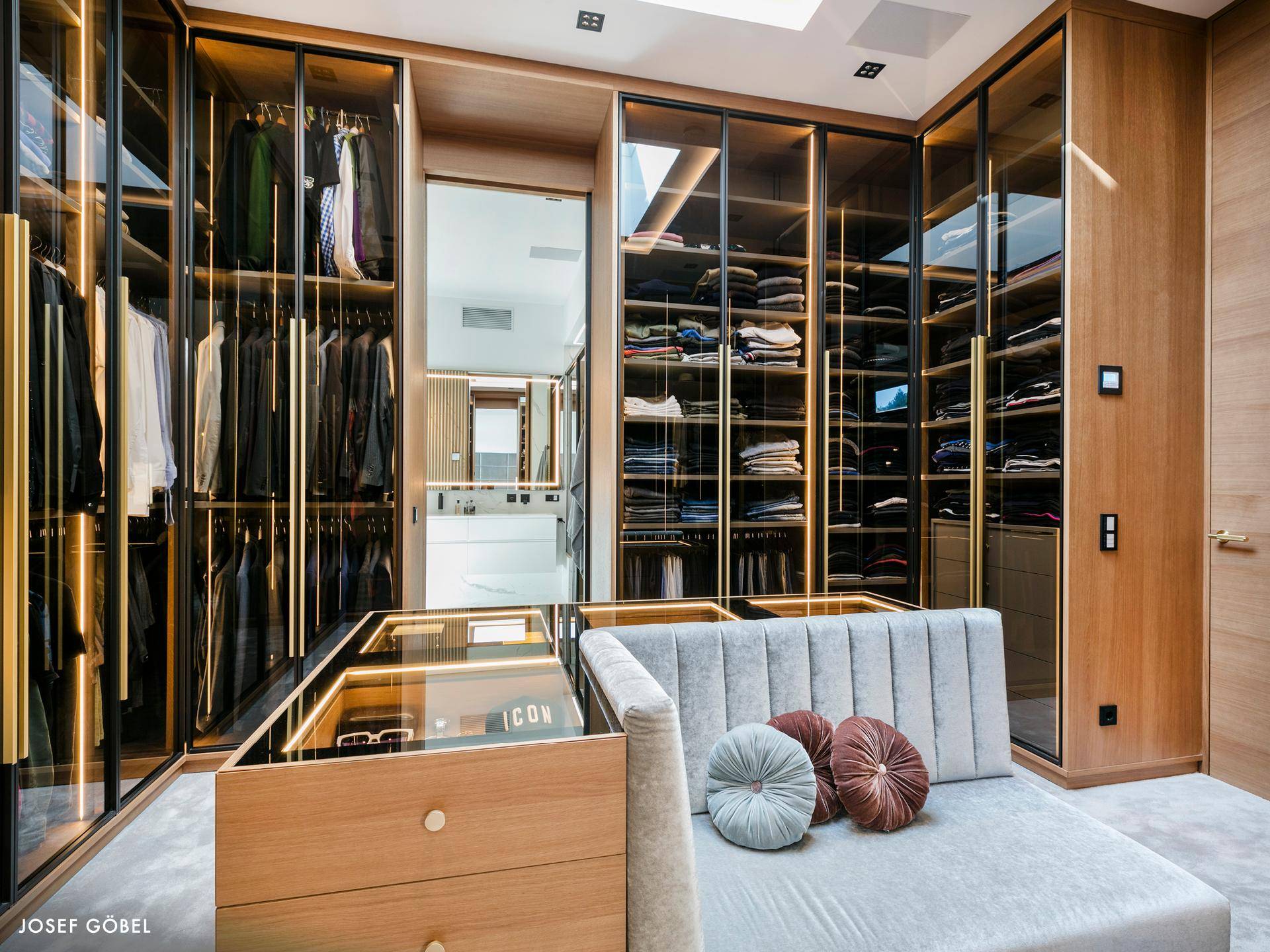Exklusiver begehbarer Kleiderschrank mit eleganten Glasfronten und integrierter Beleuchtung.