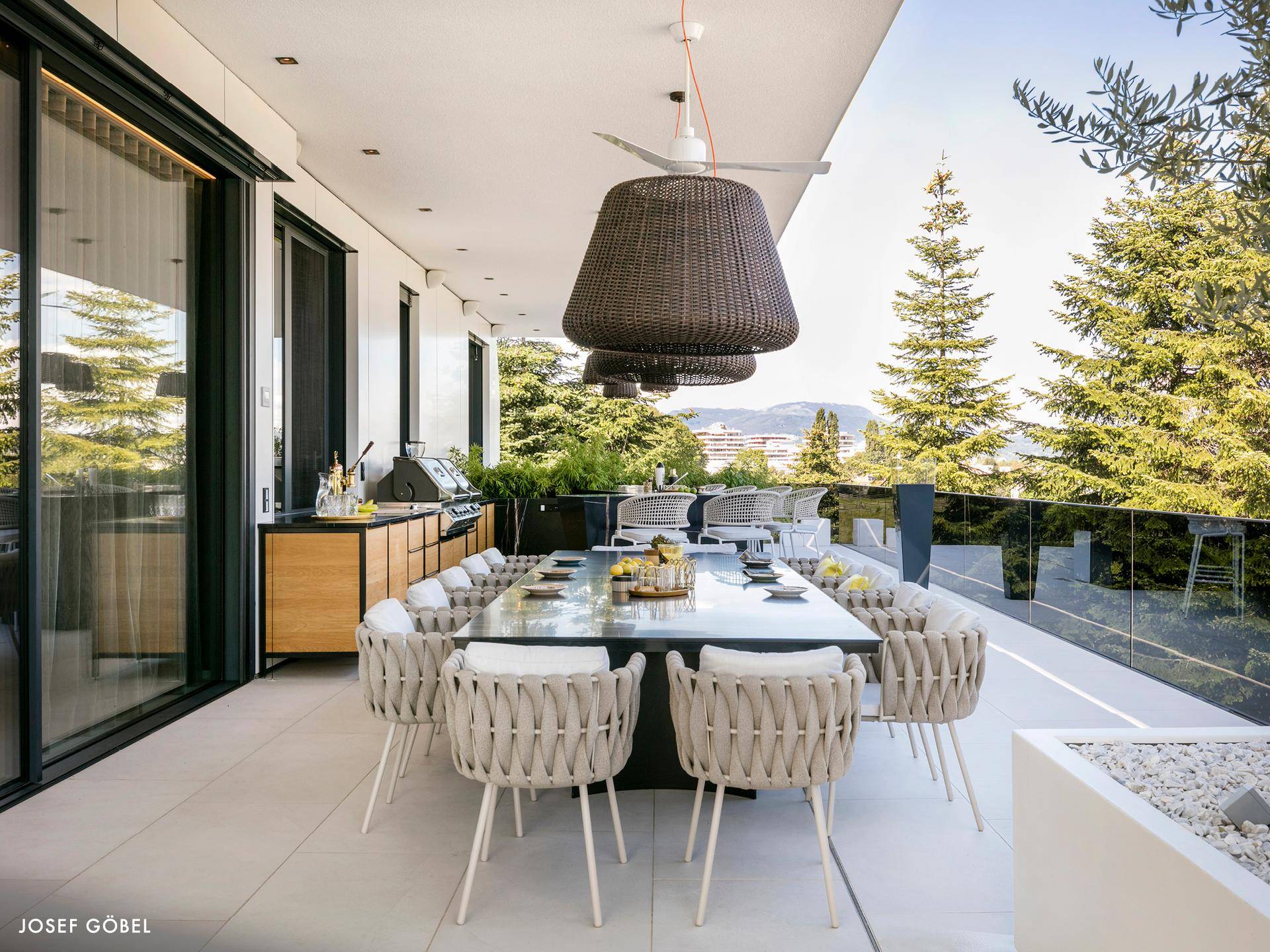 Großer Essbereich im Freien auf einer eleganten Terrasse mit Blick ins Grüne und modernen Möbeln.