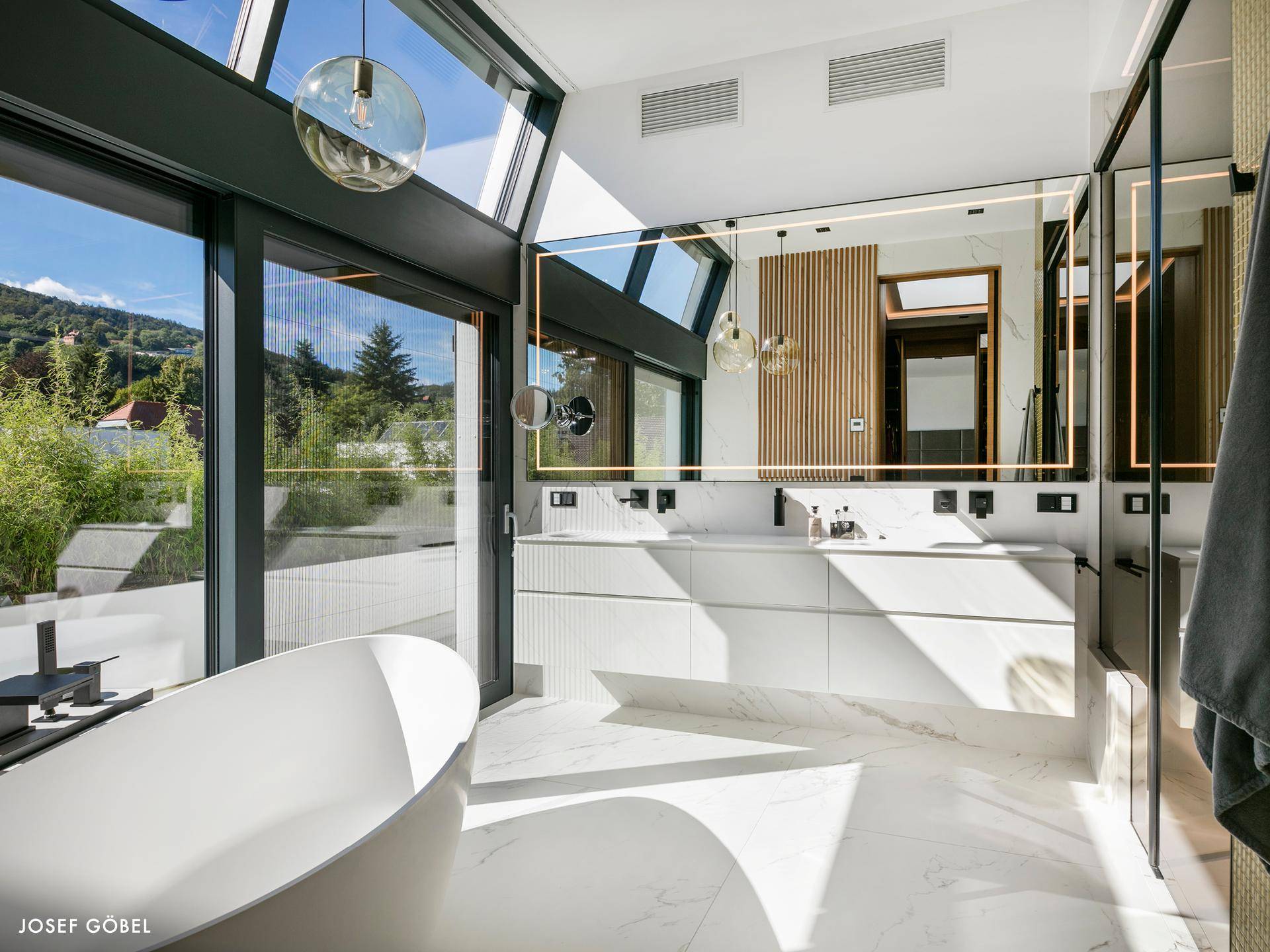 Luxuriöses Badezimmer mit freistehender Badewanne, Doppelwaschbecken und großen Fenstern mit Bergblick.