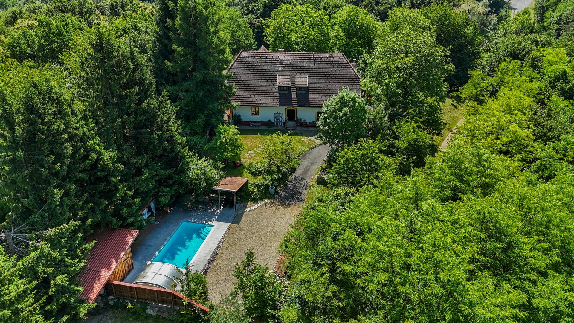 Luftaufnahme eines Hauses umgeben von dichtem Grün mit einem Swimmingpool.