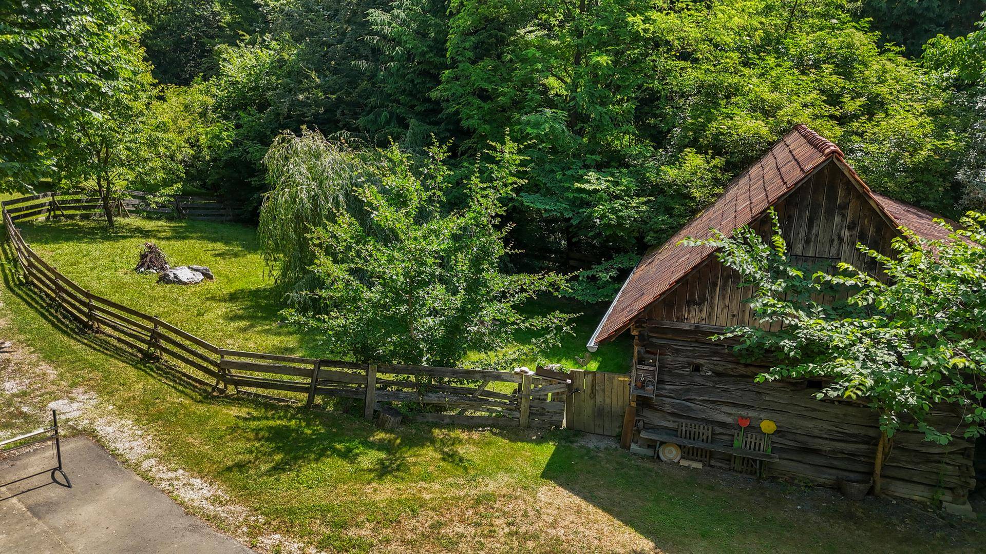 Rustikales Holzgebäude mit umzäuntem Grünbereich, eingebettet in die Natur.