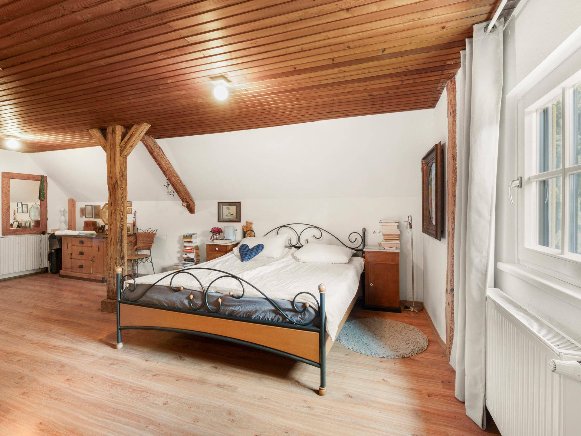 Gemütliches Schlafzimmer im Dachgeschoss mit Holzboden, schrägen Decken und Fenster.