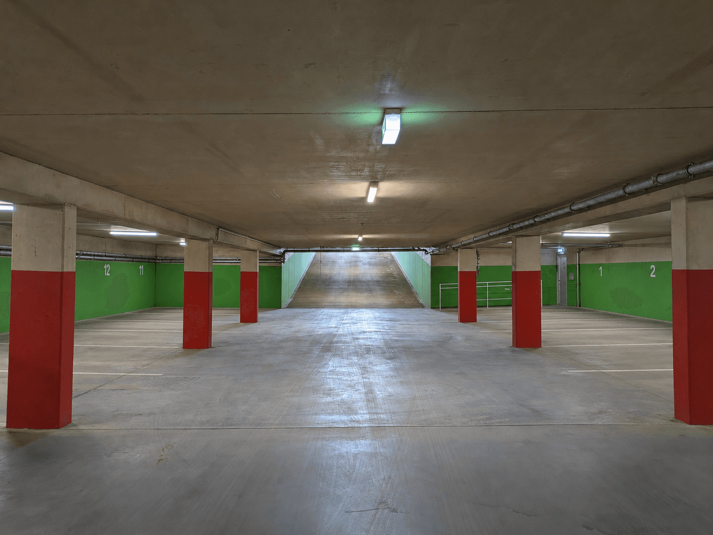 Geräumige Tiefgarage mit vielen Stellplätzen, roten Säulen und einer Rampe zur oberen Ebene.
