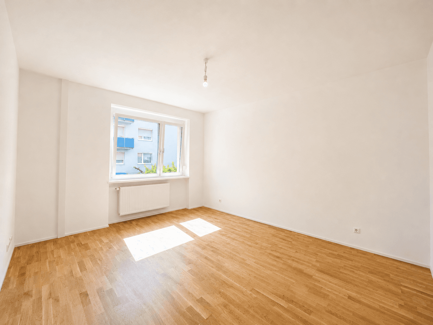 Geräumiges, helles Zimmer mit Parkettboden und einem großen Fenster, das viel Tageslicht hereinlässt.