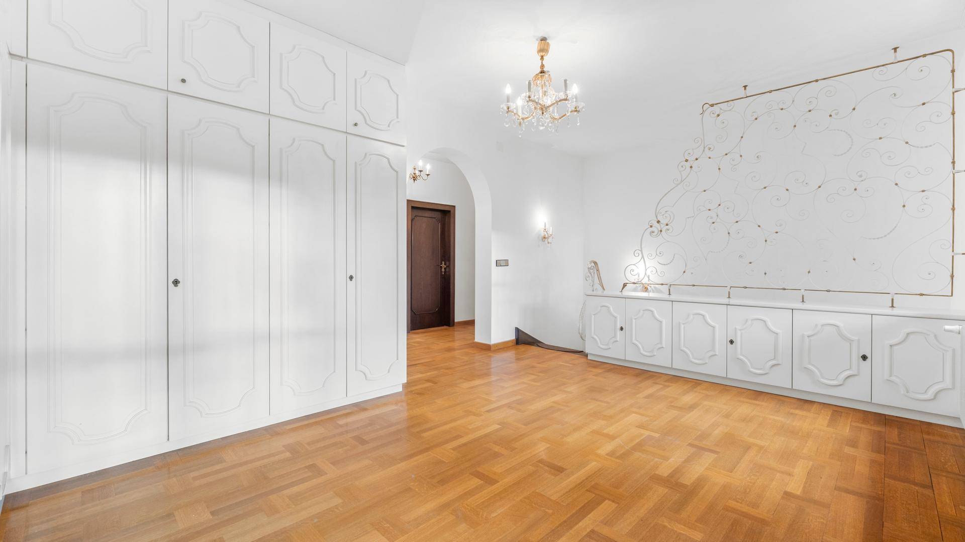 Geräumiges Zimmer mit weißen Einbauschränken, Parkettboden und dekorativer Wandgestaltung.