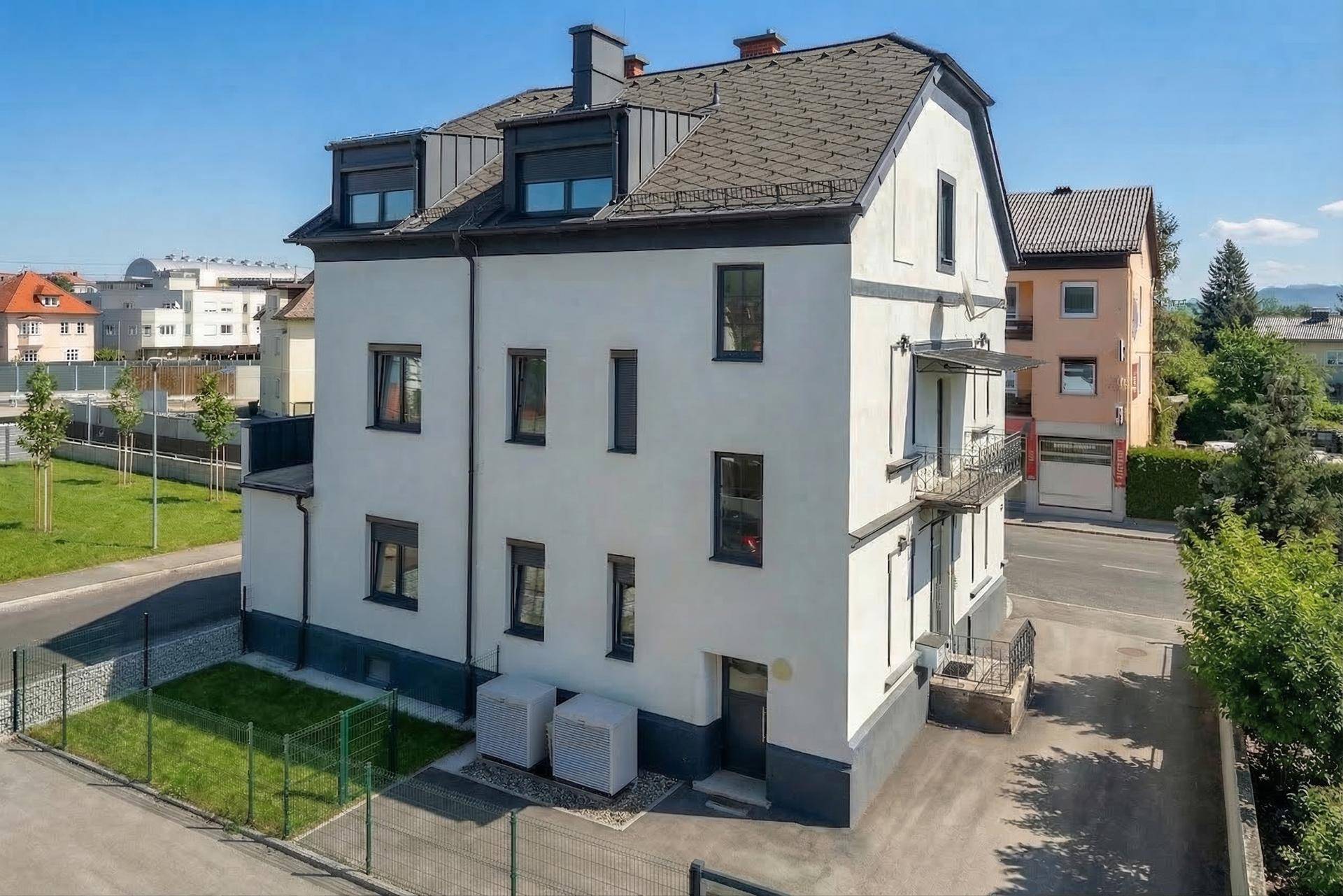Rückansicht des Gebäudes mit kleinem Gartenbereich, Balkon und Blick auf die grüne Umgebung.