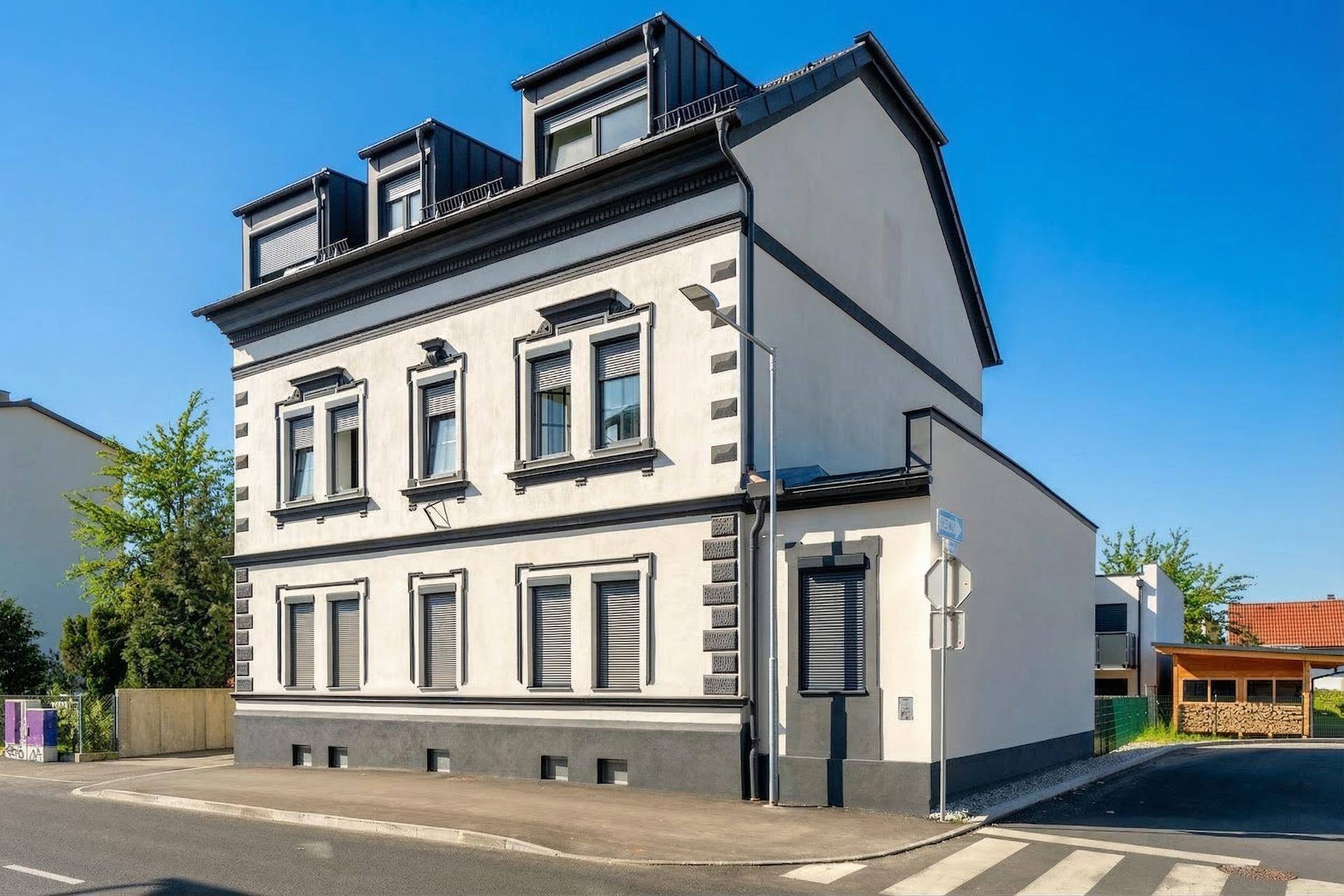 Seitenansicht des Gebäudes mit klassischer Architektur, modernen Dachdetails und Rollläden an den Fenstern.