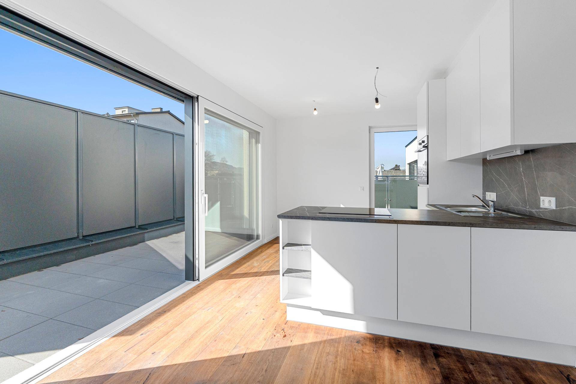 Offene Küche mit Terrassenzugang, Holzboden und modernen weißen Schränken, lichtdurchflutet.