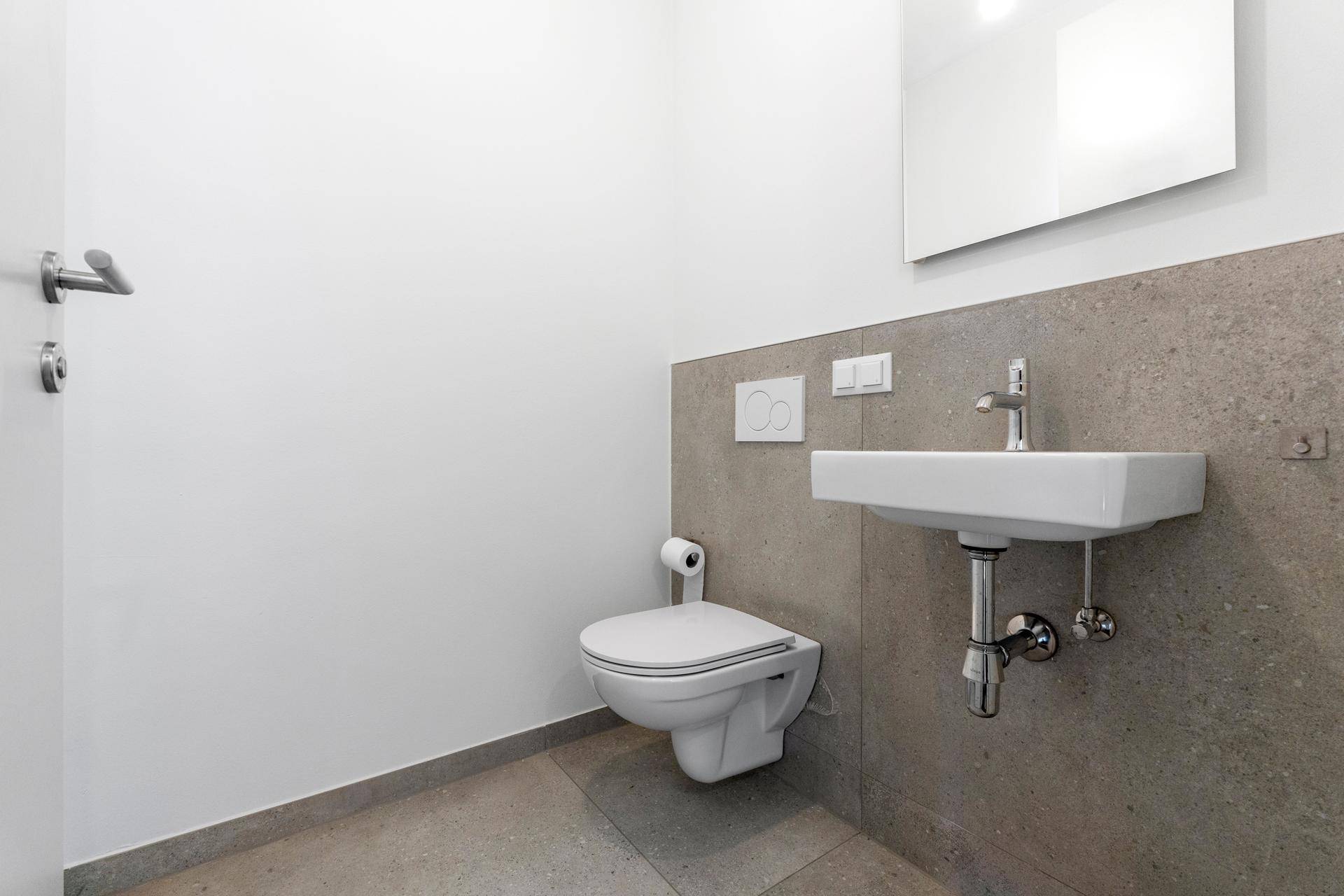 Gäste-WC mit wandhängender Toilette, kleinem Waschbecken und modernem Design in neutralen Farben.