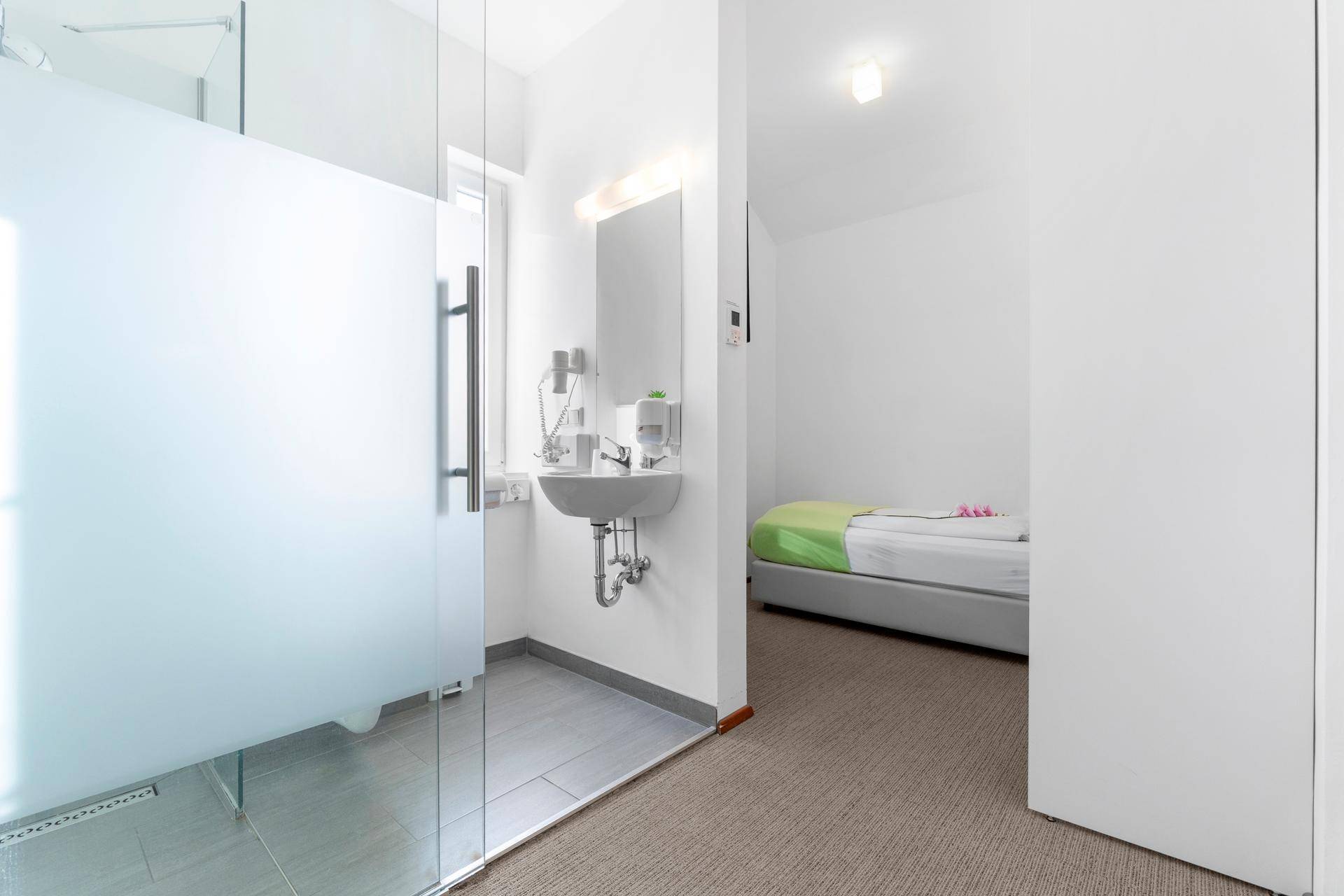Helles Schlafzimmer mit angrenzendem Badezimmer, ausgestattet mit begehbarer Dusche und Waschbecken.