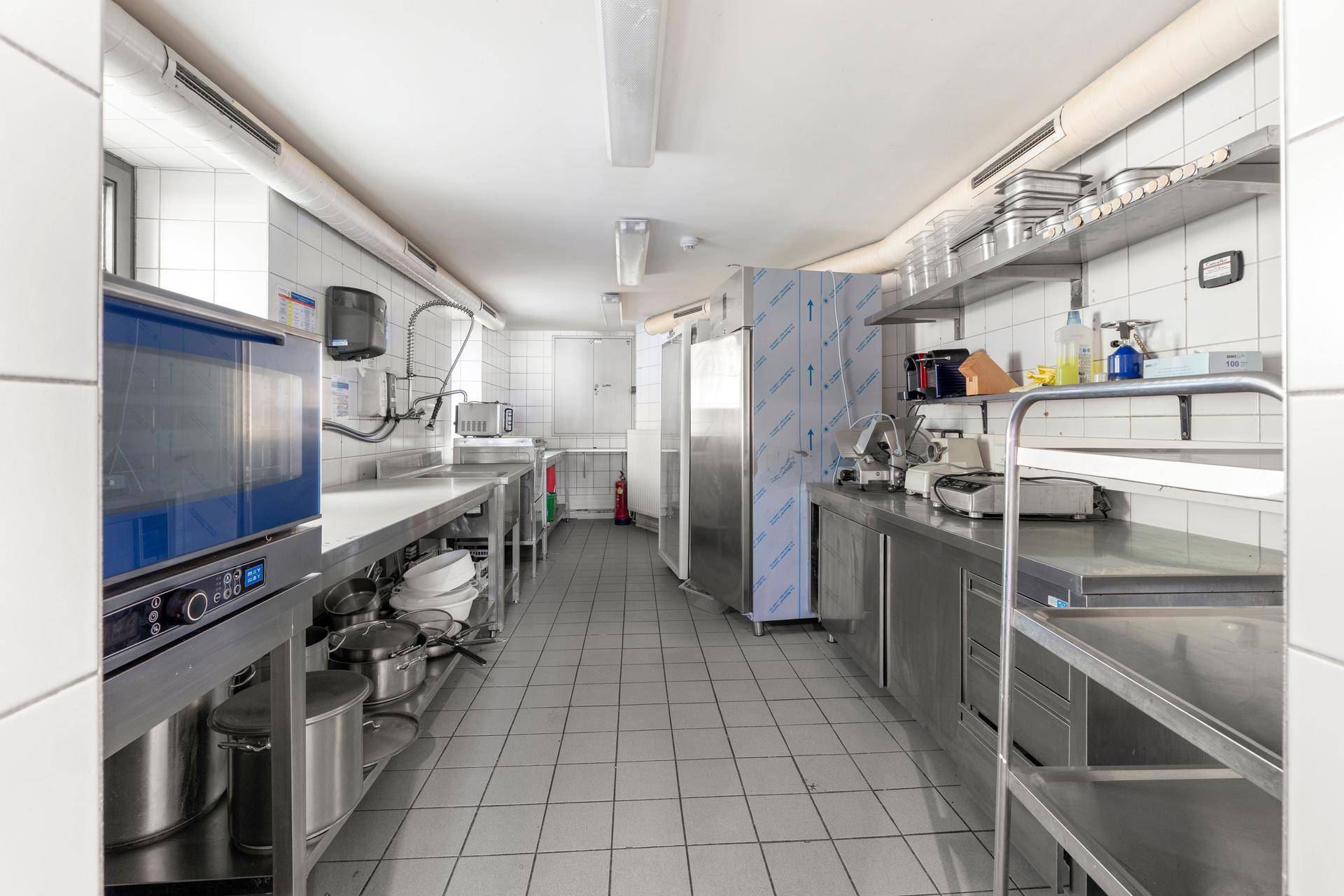 Große, professionelle Küche mit Edelstahloberflächen, Fliesenboden und umfangreicher Ausstattung für die Gastronomie.