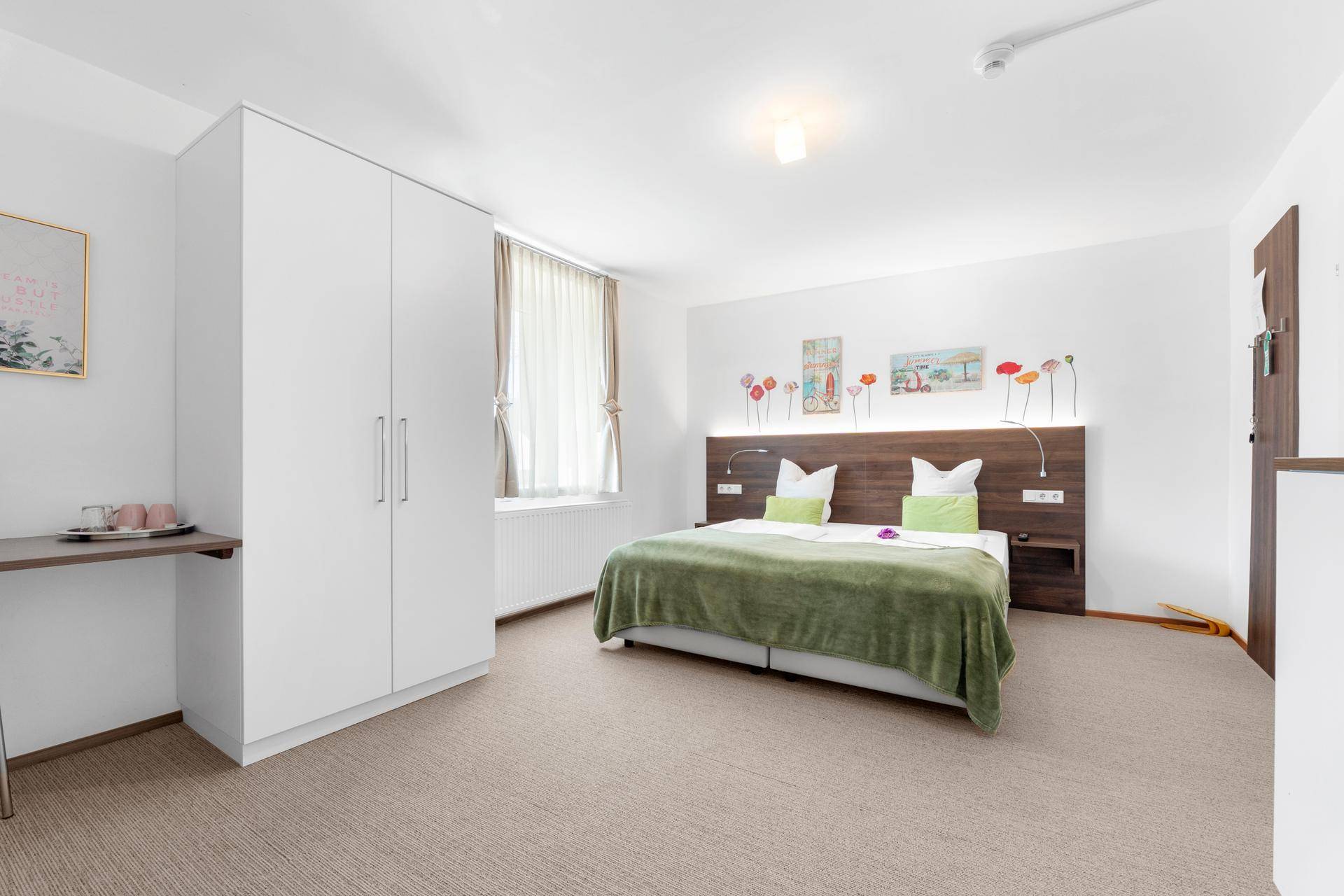 Geräumiges Schlafzimmer mit Doppelbett, weißem Kleiderschrank und kleiner Arbeitsfläche am Fenster.