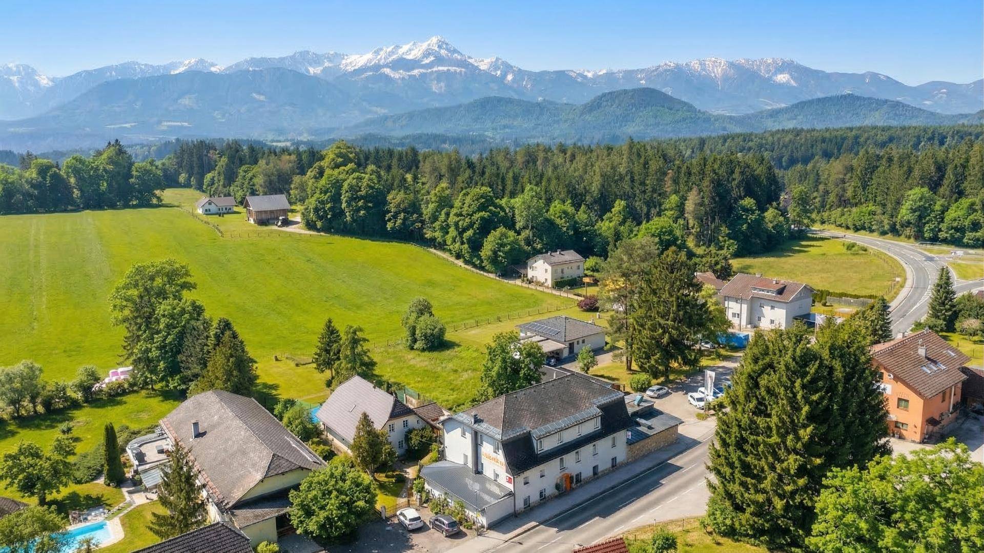 Weitläufige Luftaufnahme des Anwesens mit umliegenden Feldern, Häusern und majestätischen Bergen.