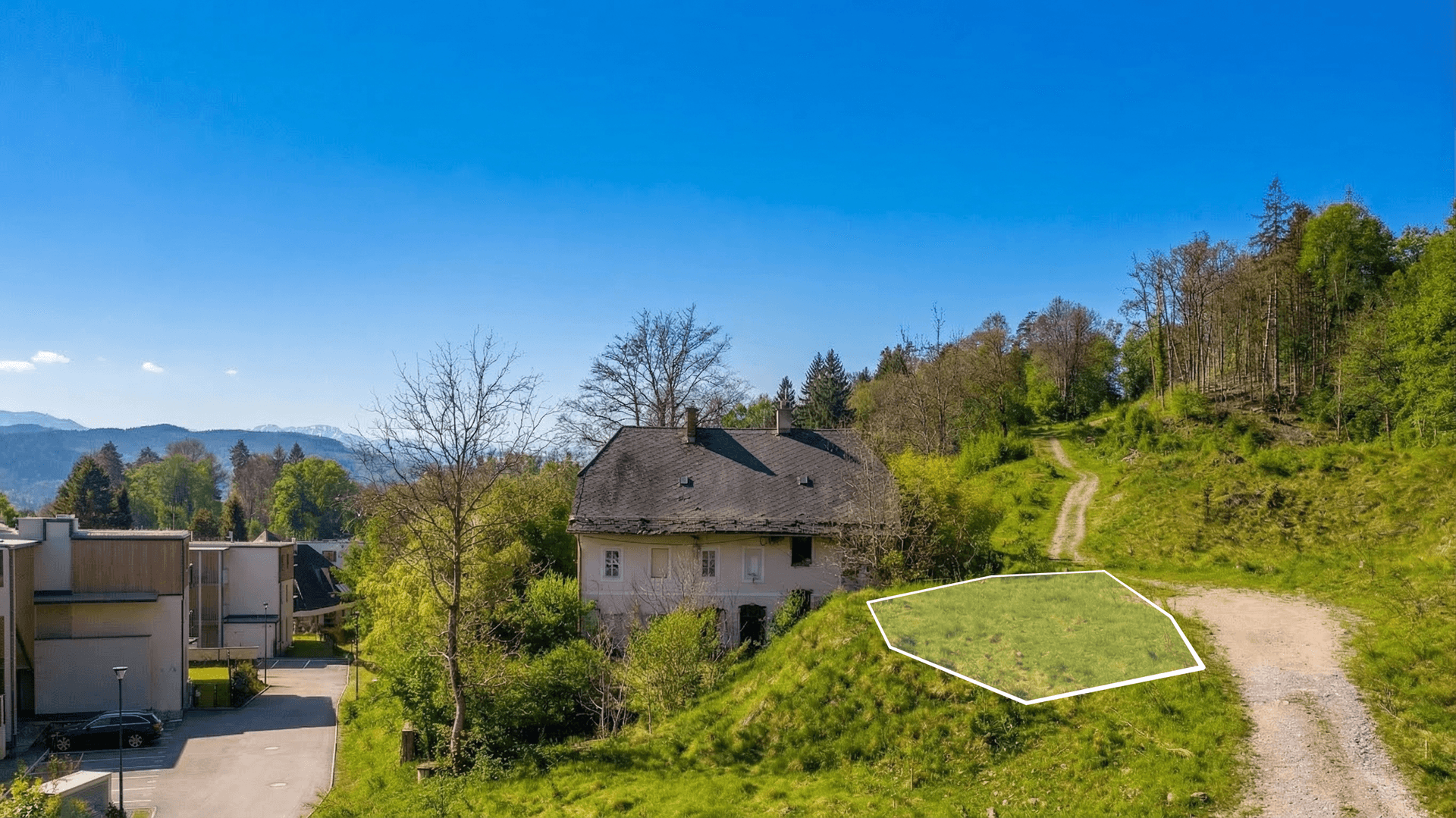 Luftaufnahme eines Hauses am Hang mit einem markierten Grundstück und Bergblick im Hintergrund.