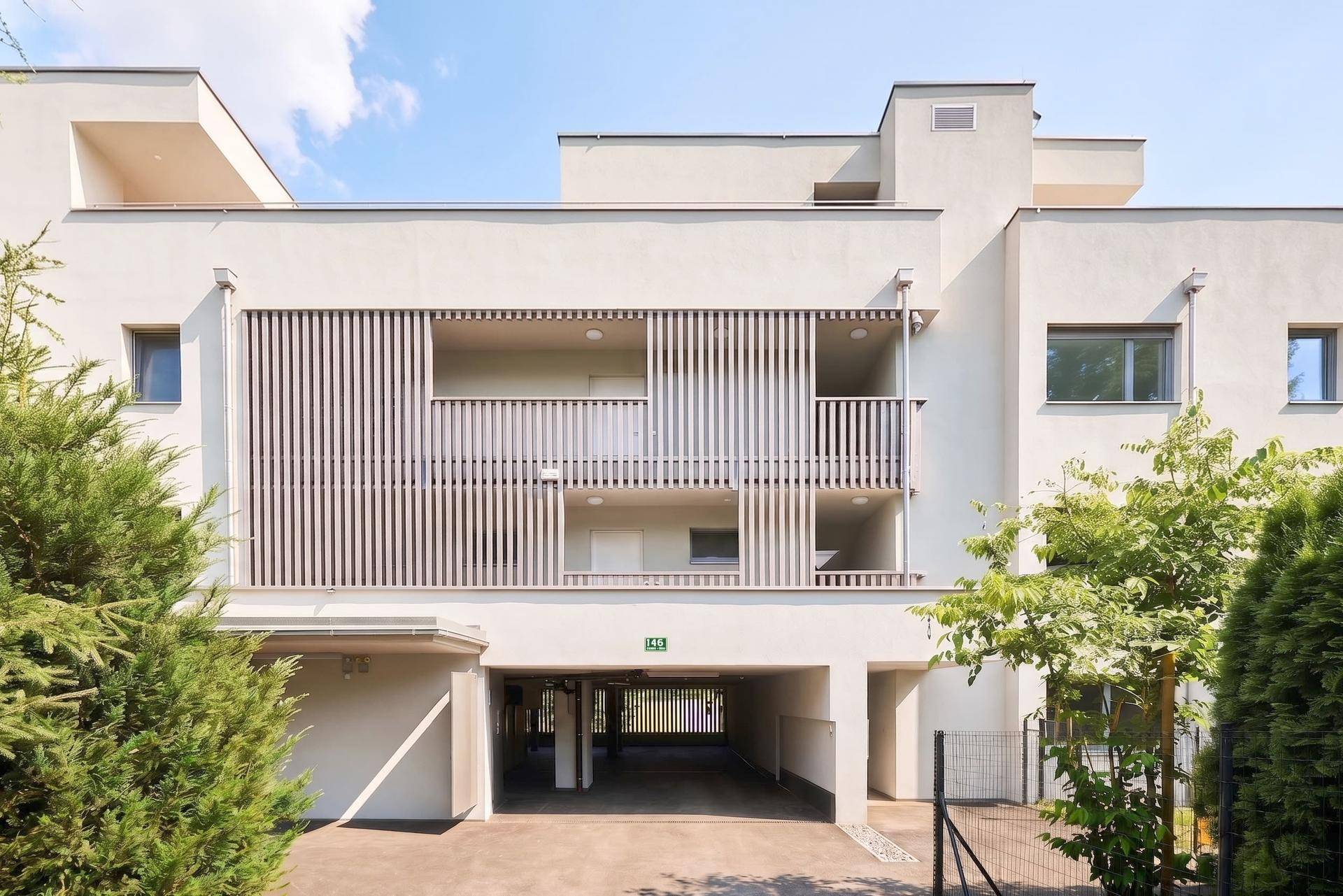 Moderne Gebäudefassade mit Balkonen und integrierter Tiefgarageneinfahrt.