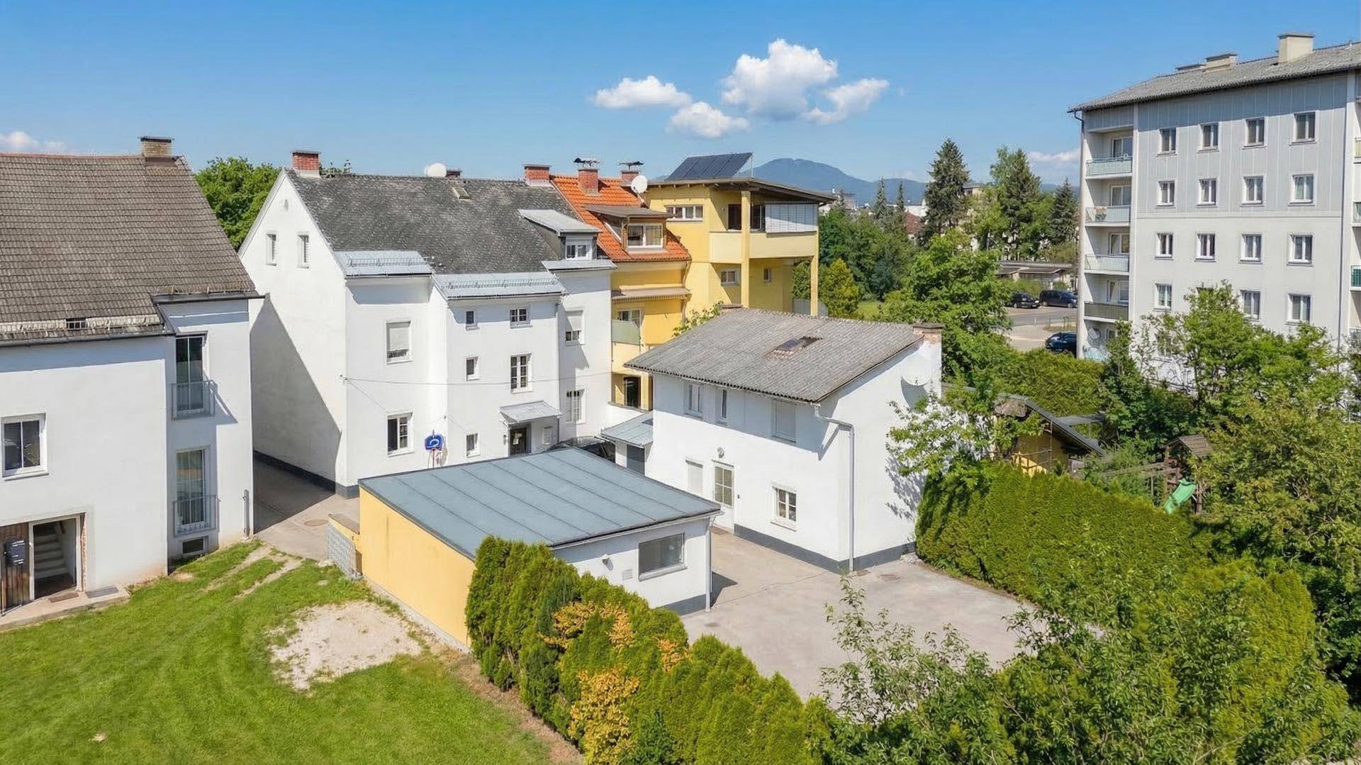 Vogelperspektive einer Wohnsiedlung mit verschiedenen Gebäuden, Grünflächen und Bergen im Hintergrund.