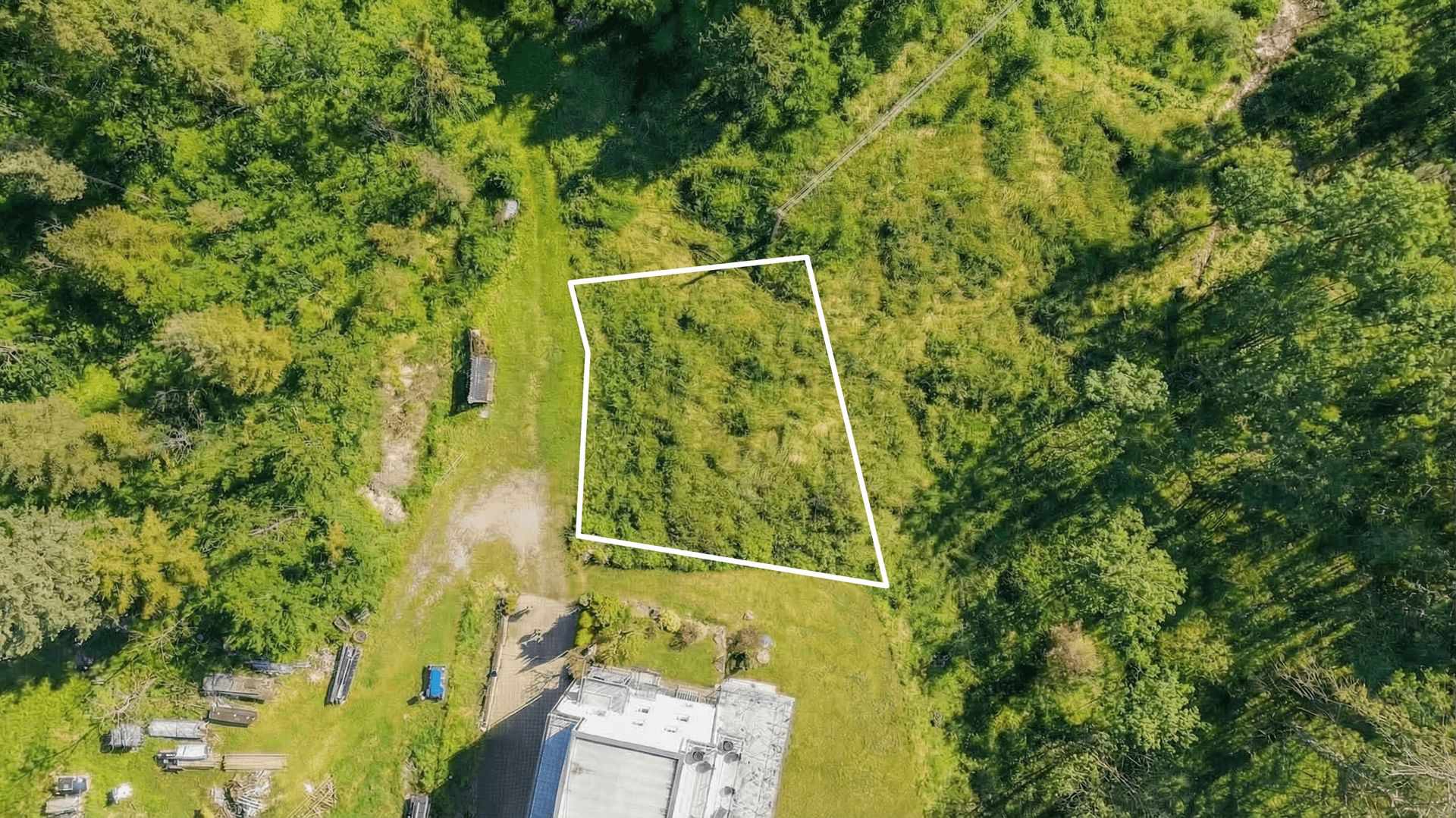 Luftaufnahme eines umrandeten Grundstücks mit dichter Vegetation und angrenzenden Gebäuden in ländlicher Lage.