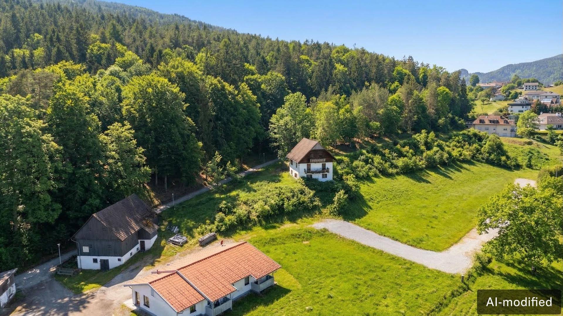Luftaufnahme von mehreren Häusern in einer grünen, hügeligen Landschaft mit viel Baumbestand und Wegen.