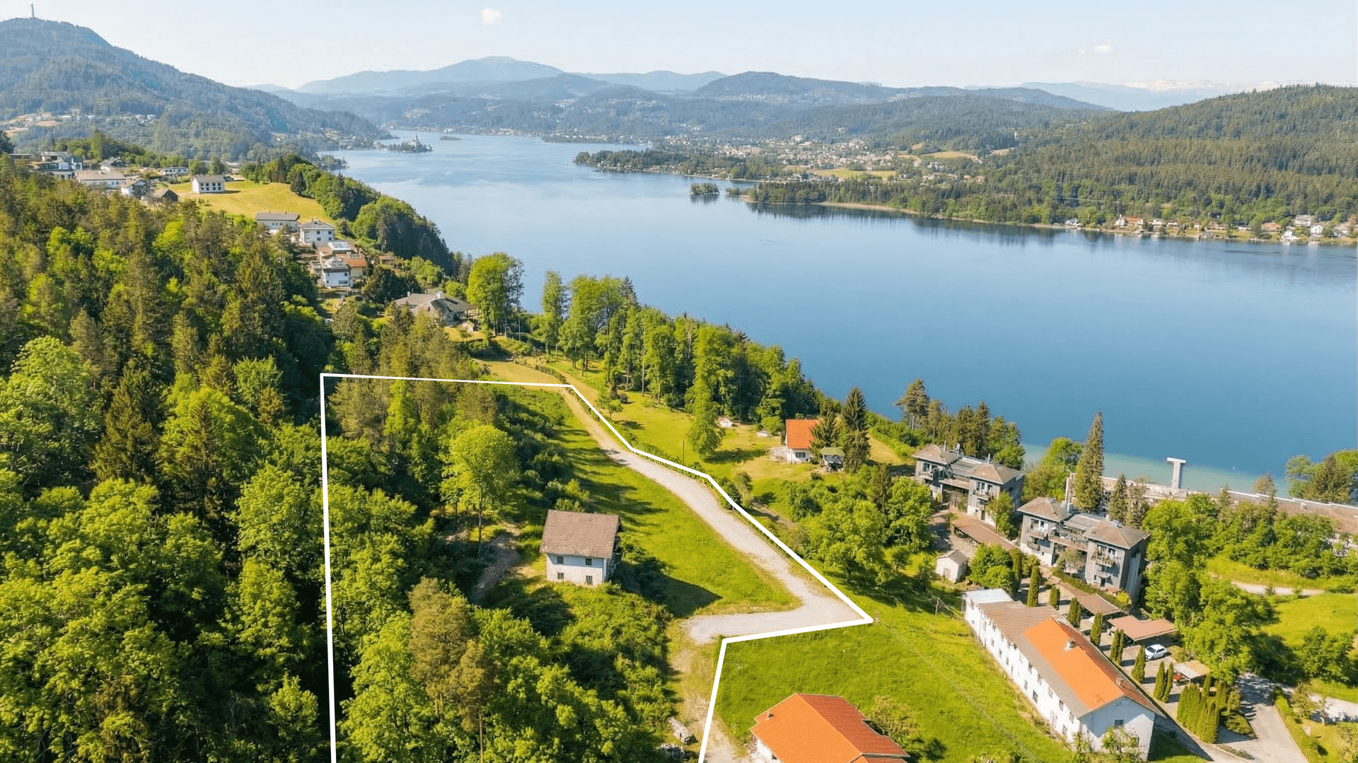 Grundstück mit Haus und Zufahrt, umrandet, mit weitem Blick auf den See und die umliegenden Berge.
