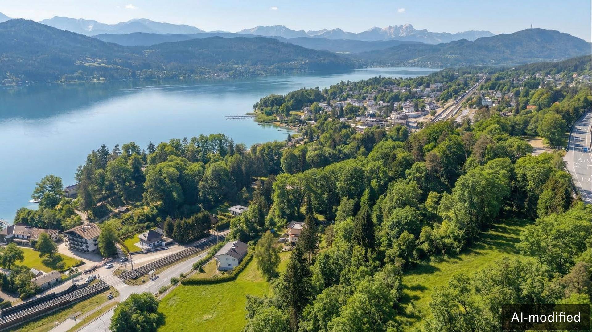 Luftaufnahme einer Siedlung am Seeufer, umgeben von üppigem Grün und einer beeindruckenden Bergkulisse.