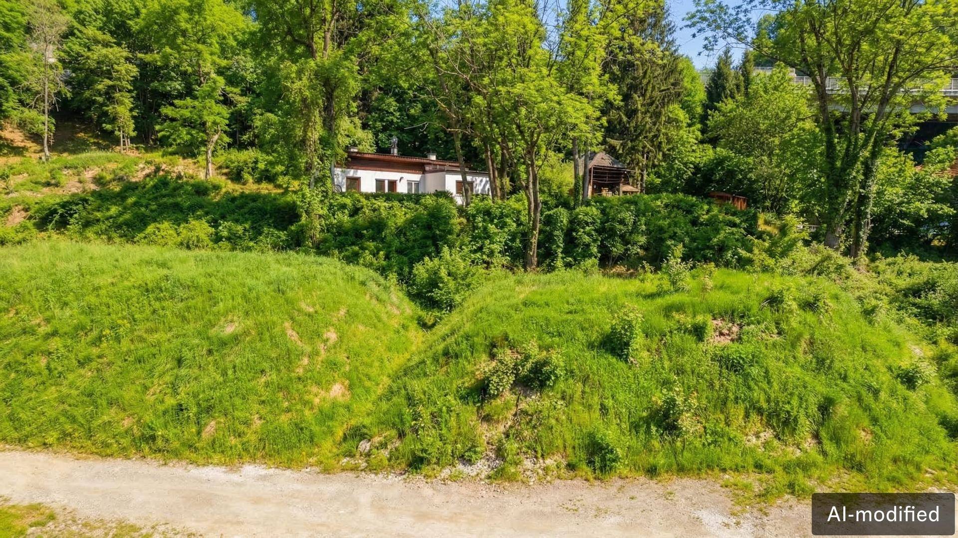 Grüne, hügelige Landschaft mit Bäumen und einem Wohnhaus im Hintergrund unter strahlendem Himmel.
