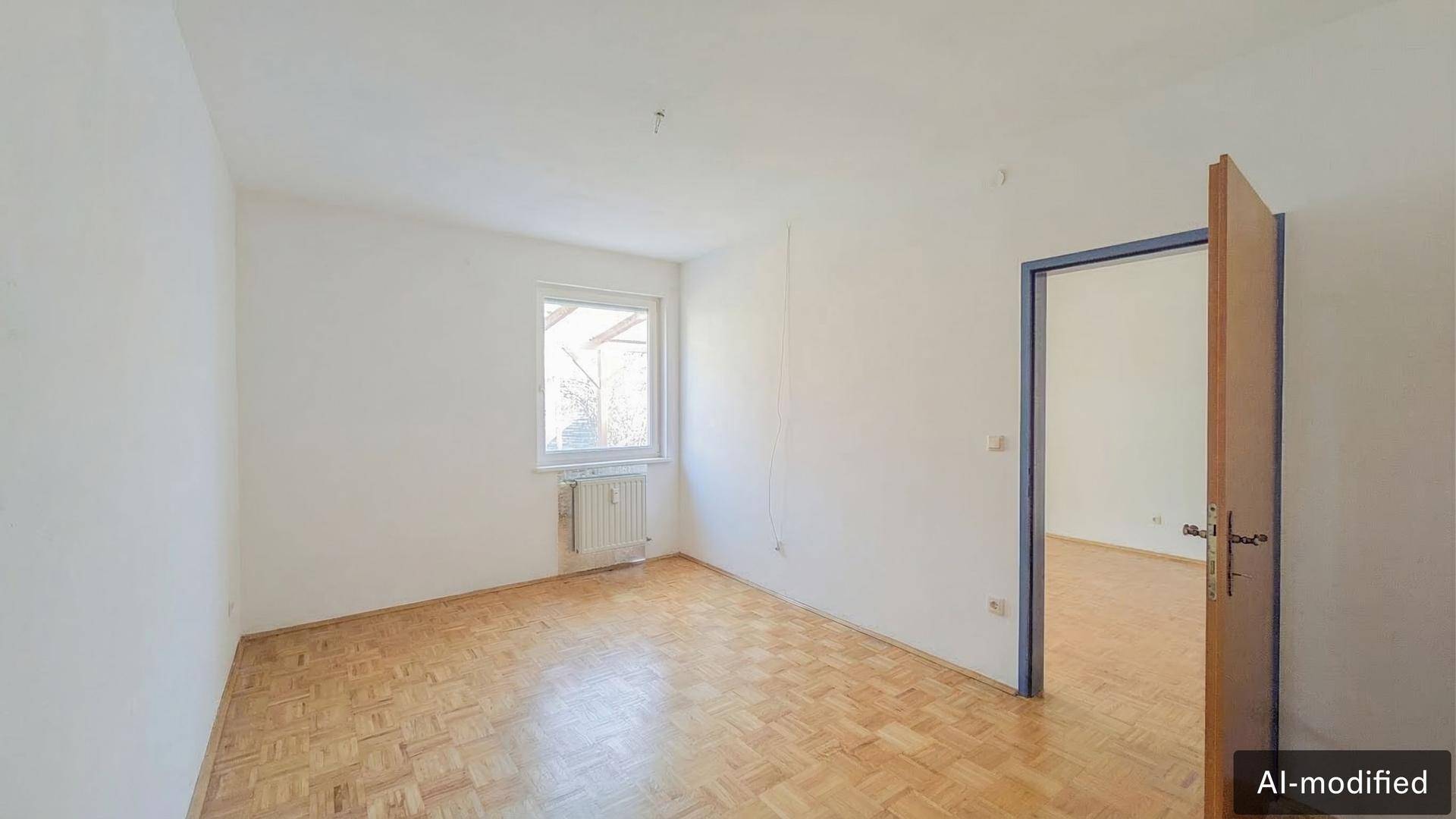 Leeres Schlafzimmer mit Parkettboden, einem Fenster und weiß gestrichenen Wänden.