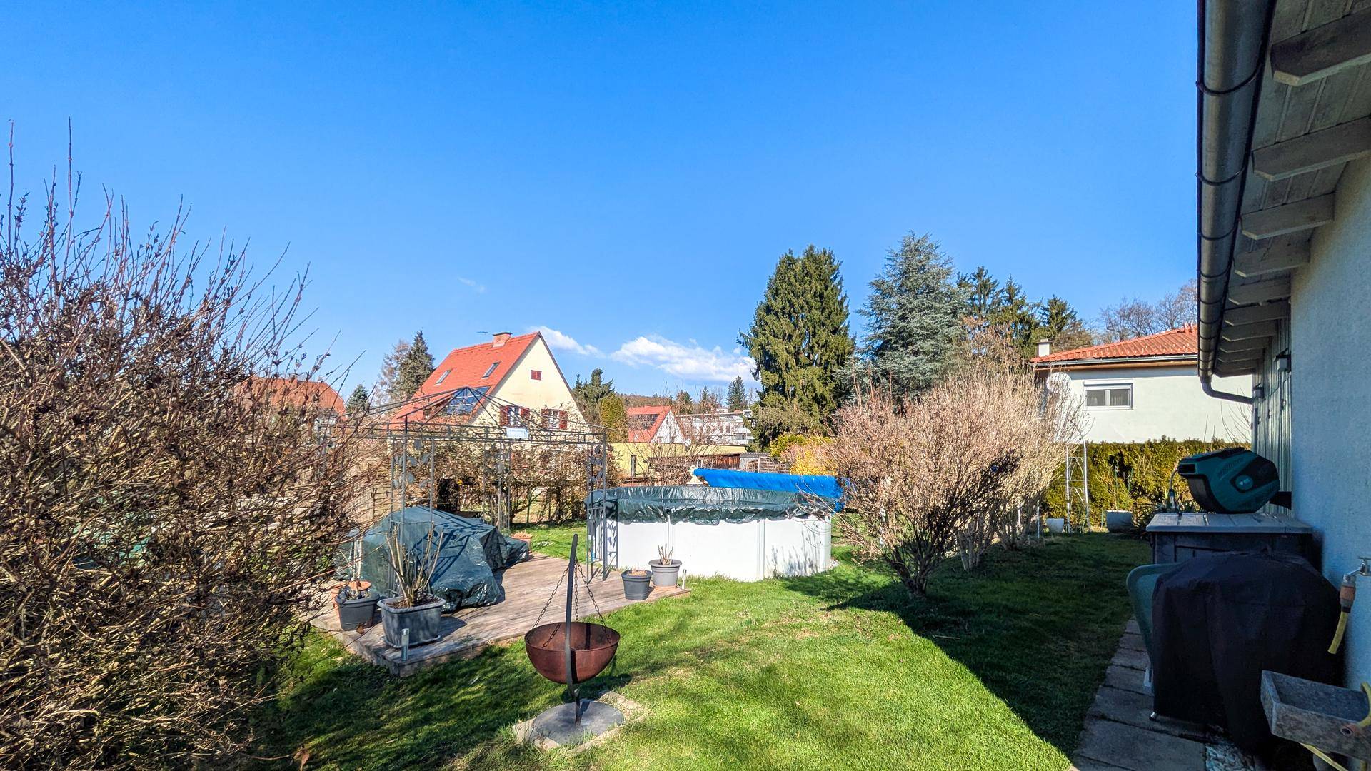 Großer Garten mit Rasenfläche, einem Aufstellpool und einer Feuerstelle im Freien.