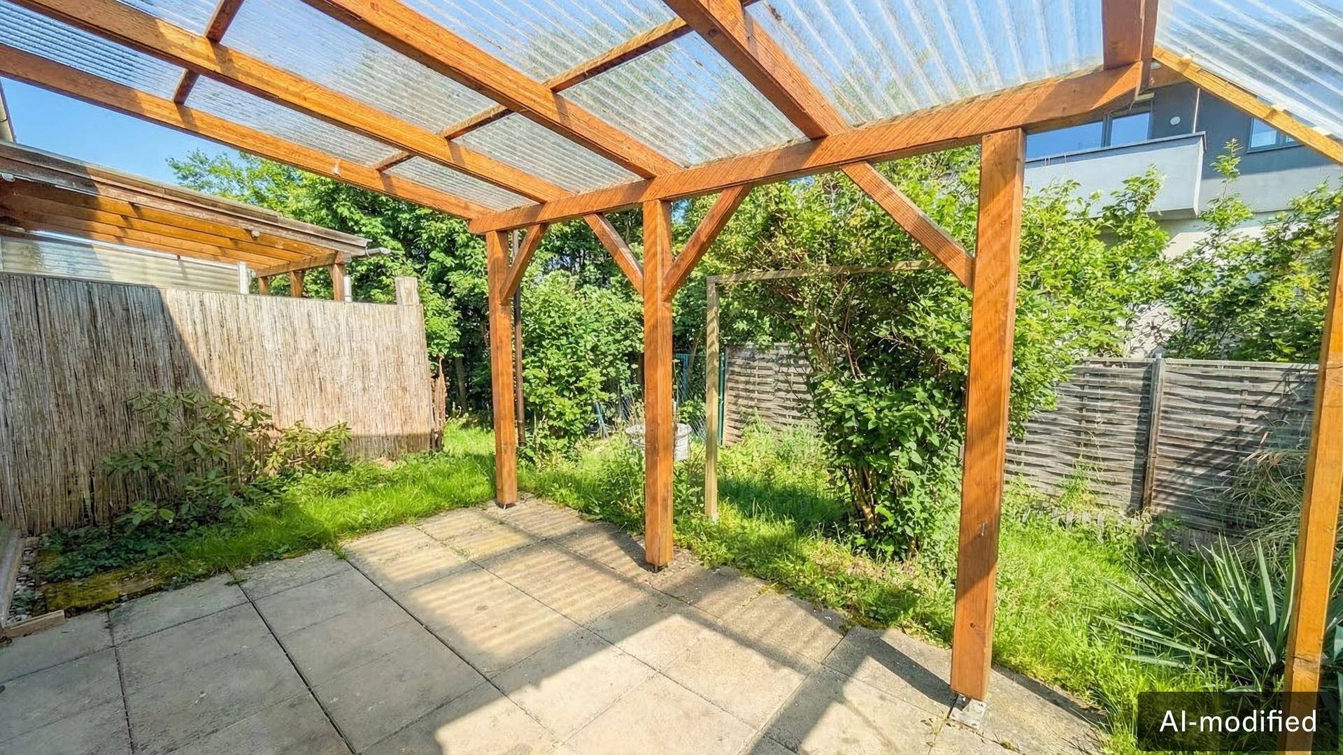 Überdachte Terrasse mit Holzpergola und gepflastertem Boden, umgeben von Grünflächen.