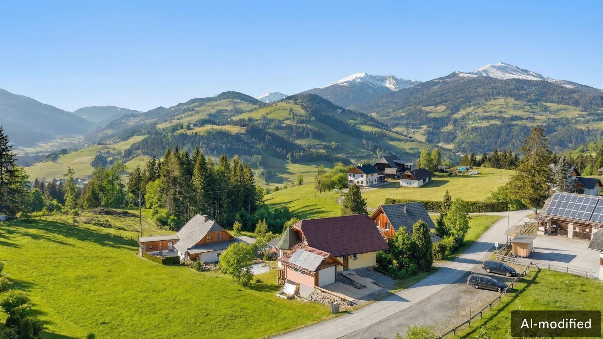 Panoramablick auf die ländliche Umgebung mit Häusern, grünen Hügeln und schneebedeckten Bergen.
