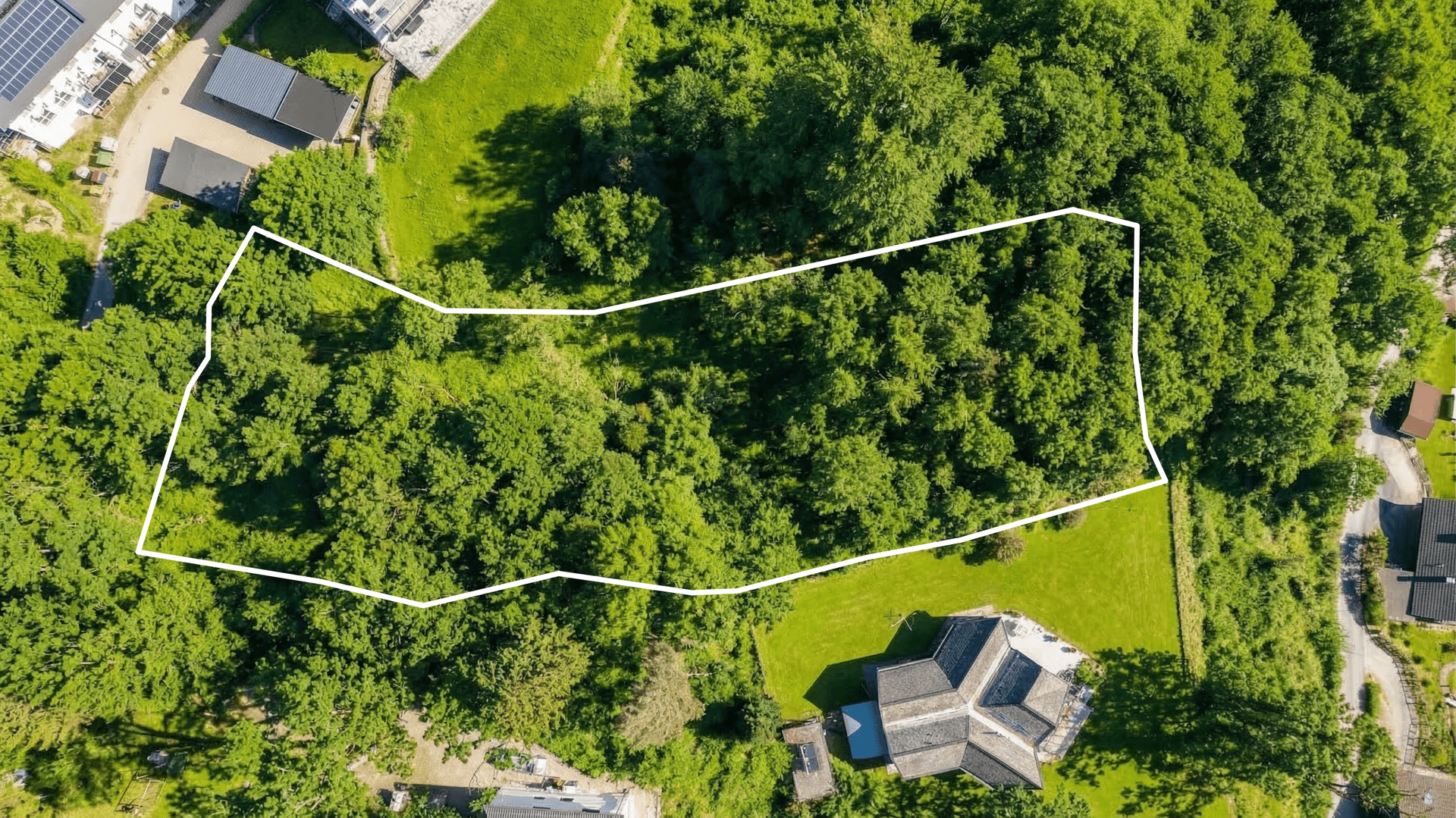 Luftaufnahme eines großen, unregelmäßig geformten Grundstücks, umgeben von dichtem Wald und Grünflächen.