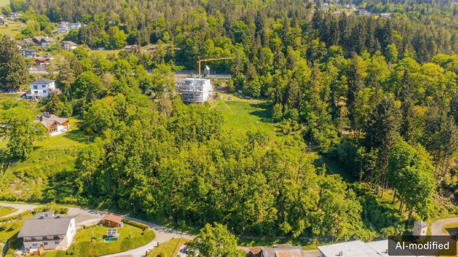 Luftaufnahme einer bewaldeten Hügellandschaft mit Wohnhäusern und einer Baustelle im Hintergrund.