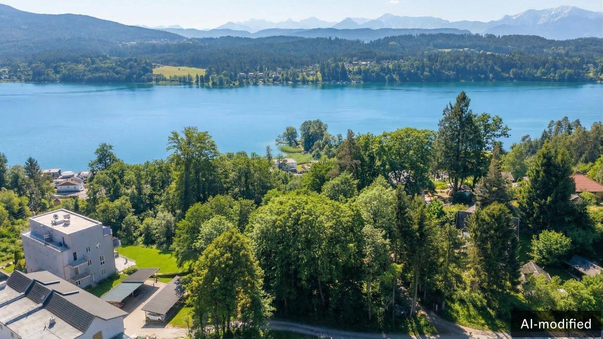 Weitläufiger Blick auf einen See mit Bergen, umgeben von Wäldern und modernen Wohngebäuden.
