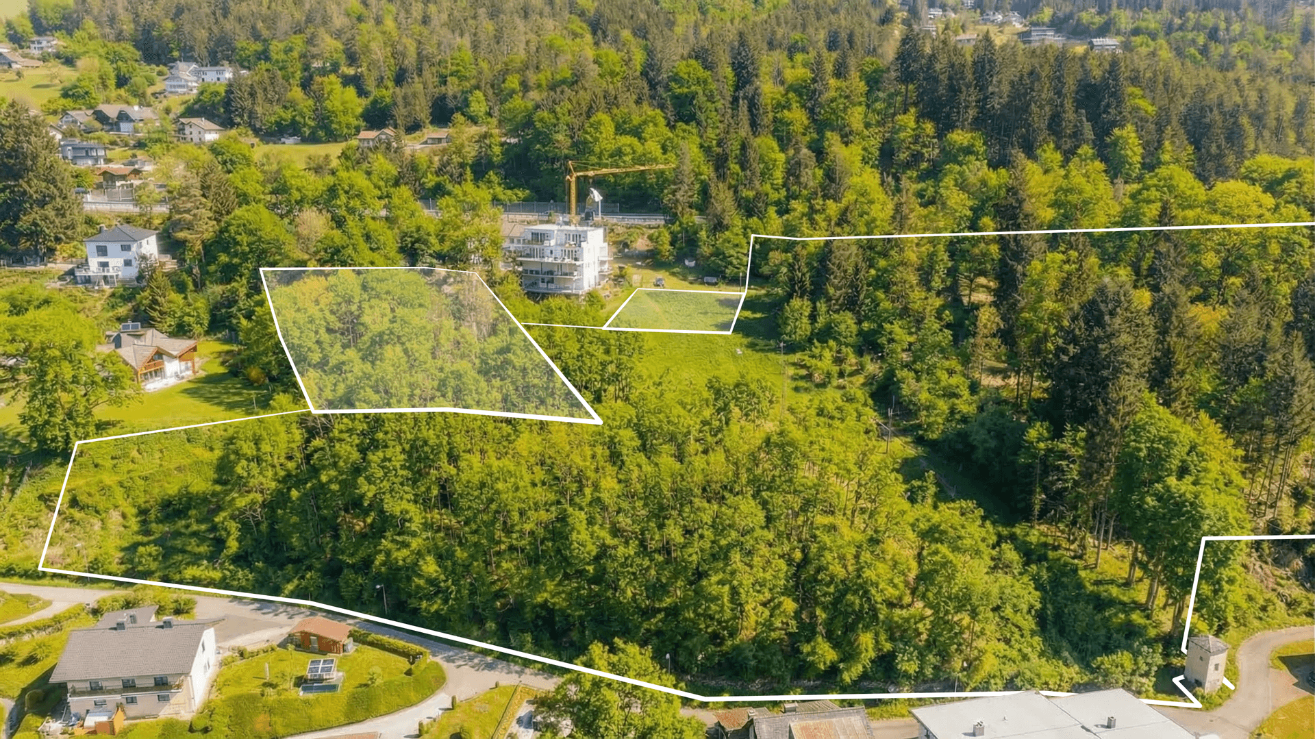 Luftaufnahme einer grünen Hügellandschaft mit mehreren markierten Grundstücken und einer Baustelle.