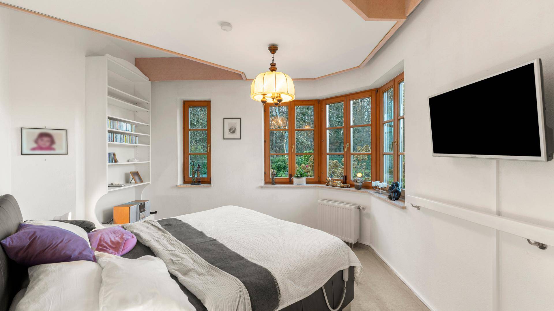 Gemütliches Schlafzimmer mit großem Erkerfenster, Doppelbett und Wandfernseher.