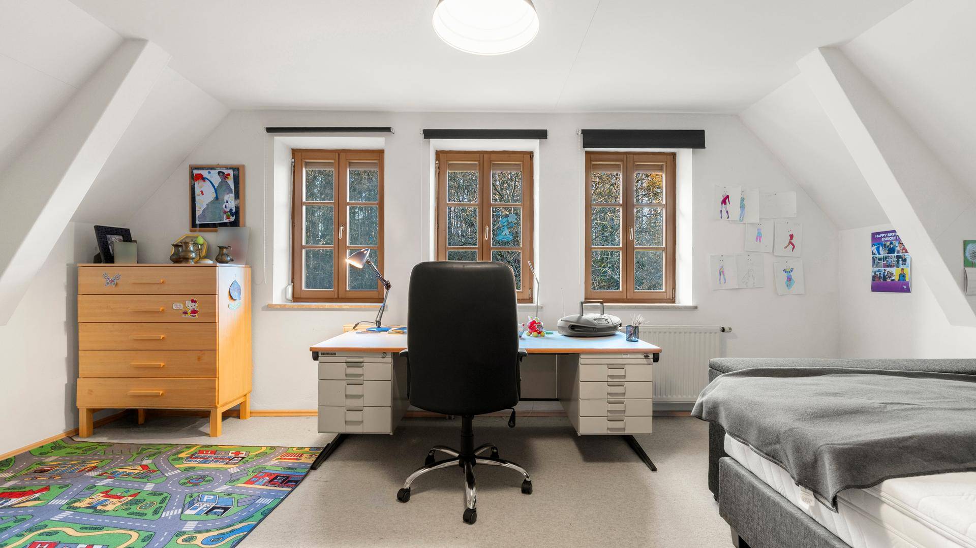 Helles Dachzimmer mit Schreibtisch, Bett und schrägen Decken, ideal als Kinder- oder Arbeitszimmer.