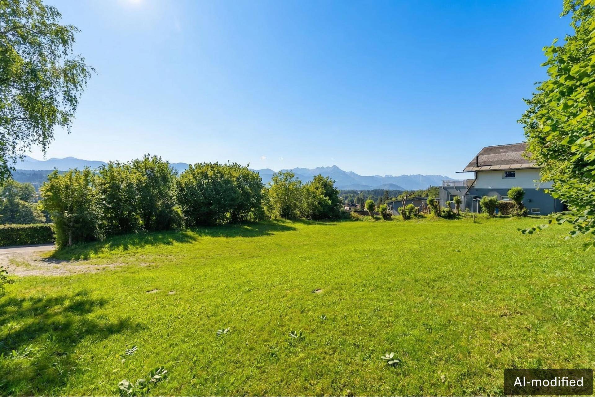 Weitläufiger grüner Rasen mit Sträuchern und einem Haus im Hintergrund, umgeben von einer malerischen Berglandschaft.