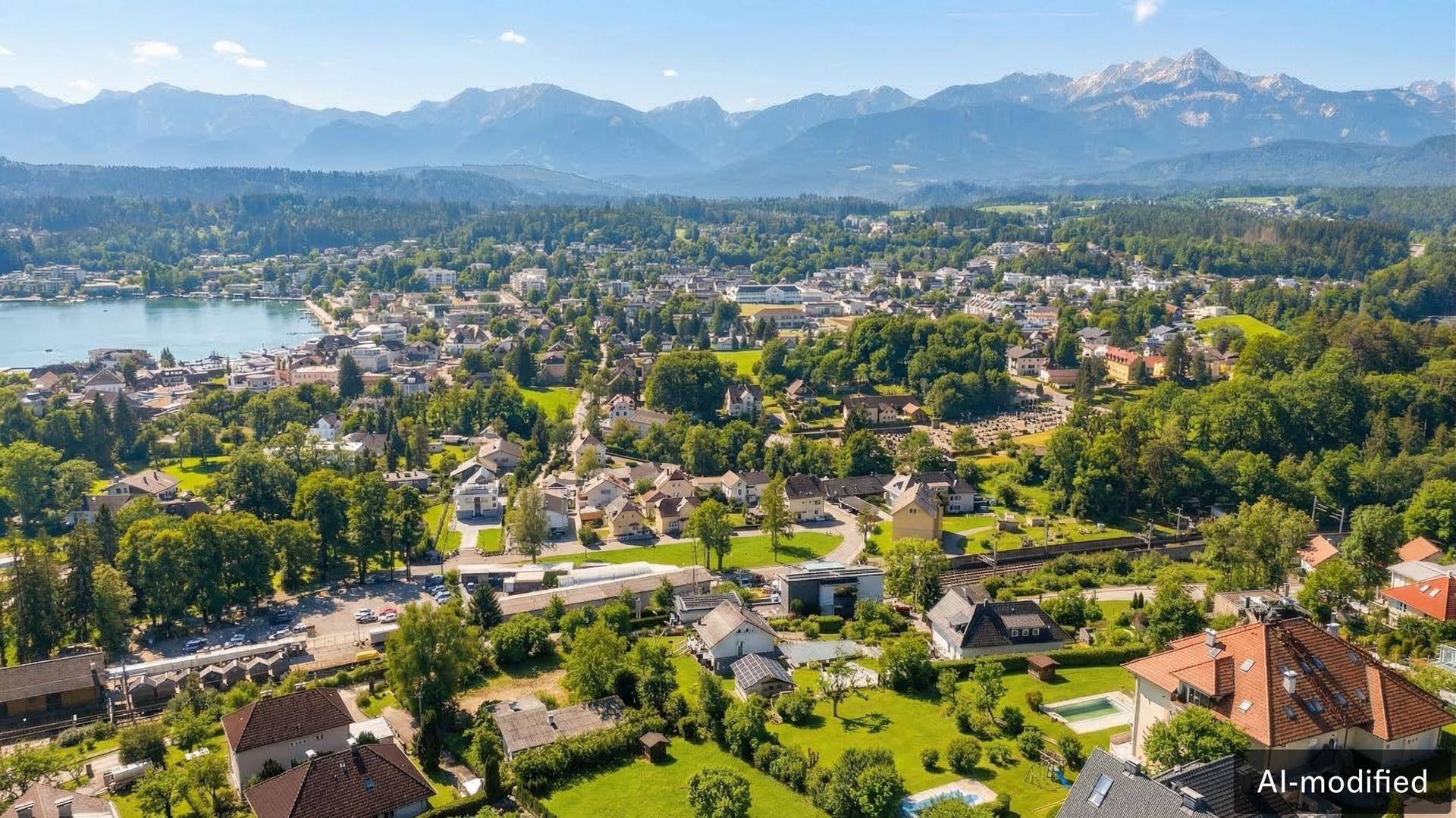 Weitläufige Luftaufnahme einer Stadt mit vielen Häusern, grünen Flächen, einem See und einer beeindruckenden Bergkulisse.