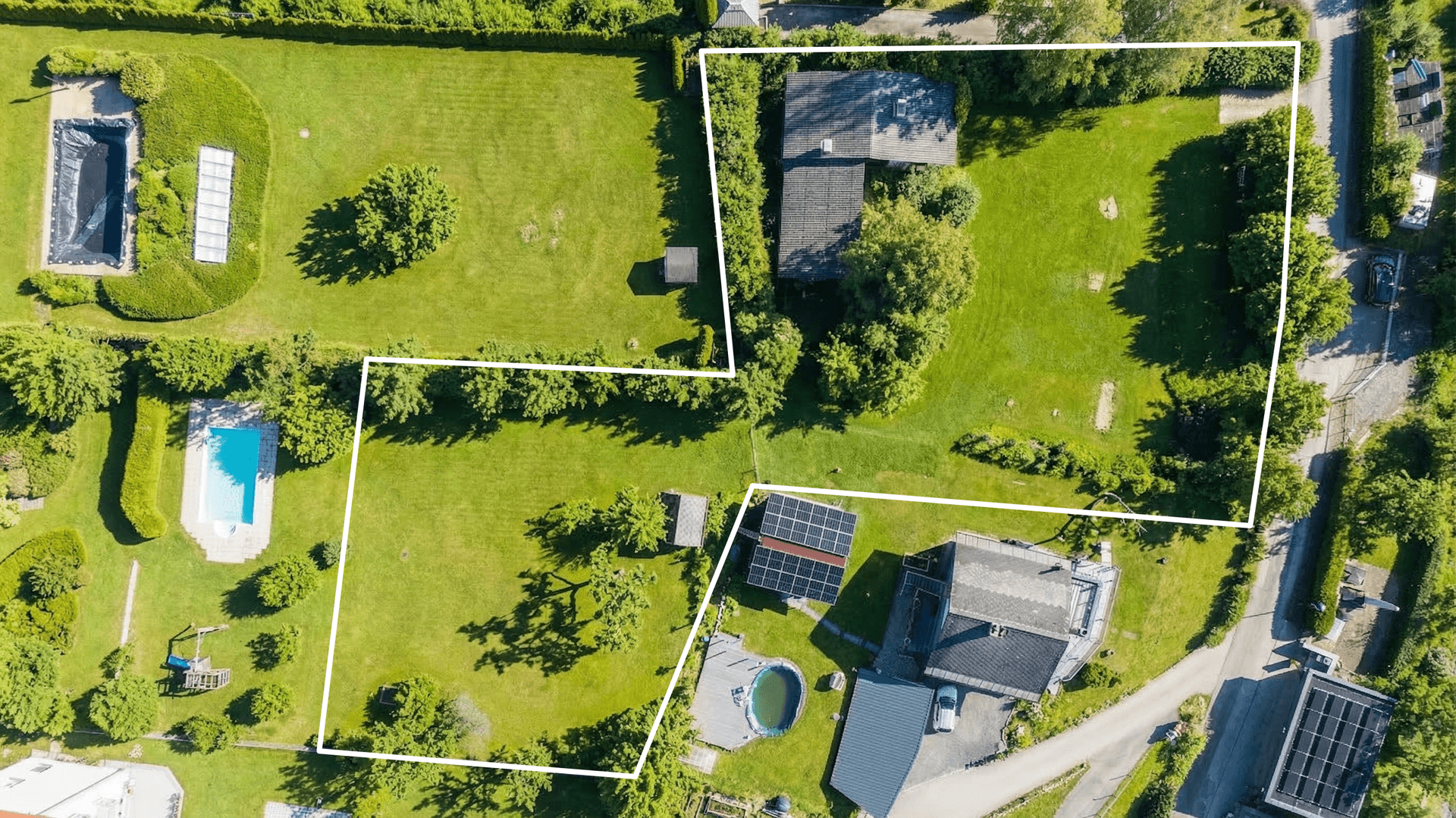 Luftaufnahme von mehreren Grundstücken mit Häusern, grünen Gärten, einem Pool und Solaranlagen auf einem Dach.