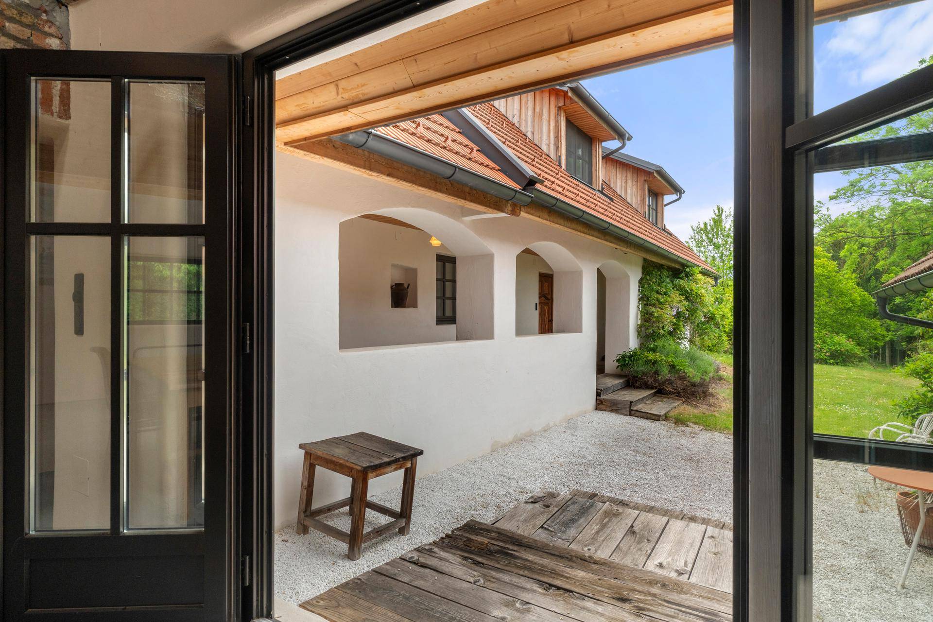 Sonniger Außenbereich mit Holzboden, Kiesfläche und Zugang zum Garten.