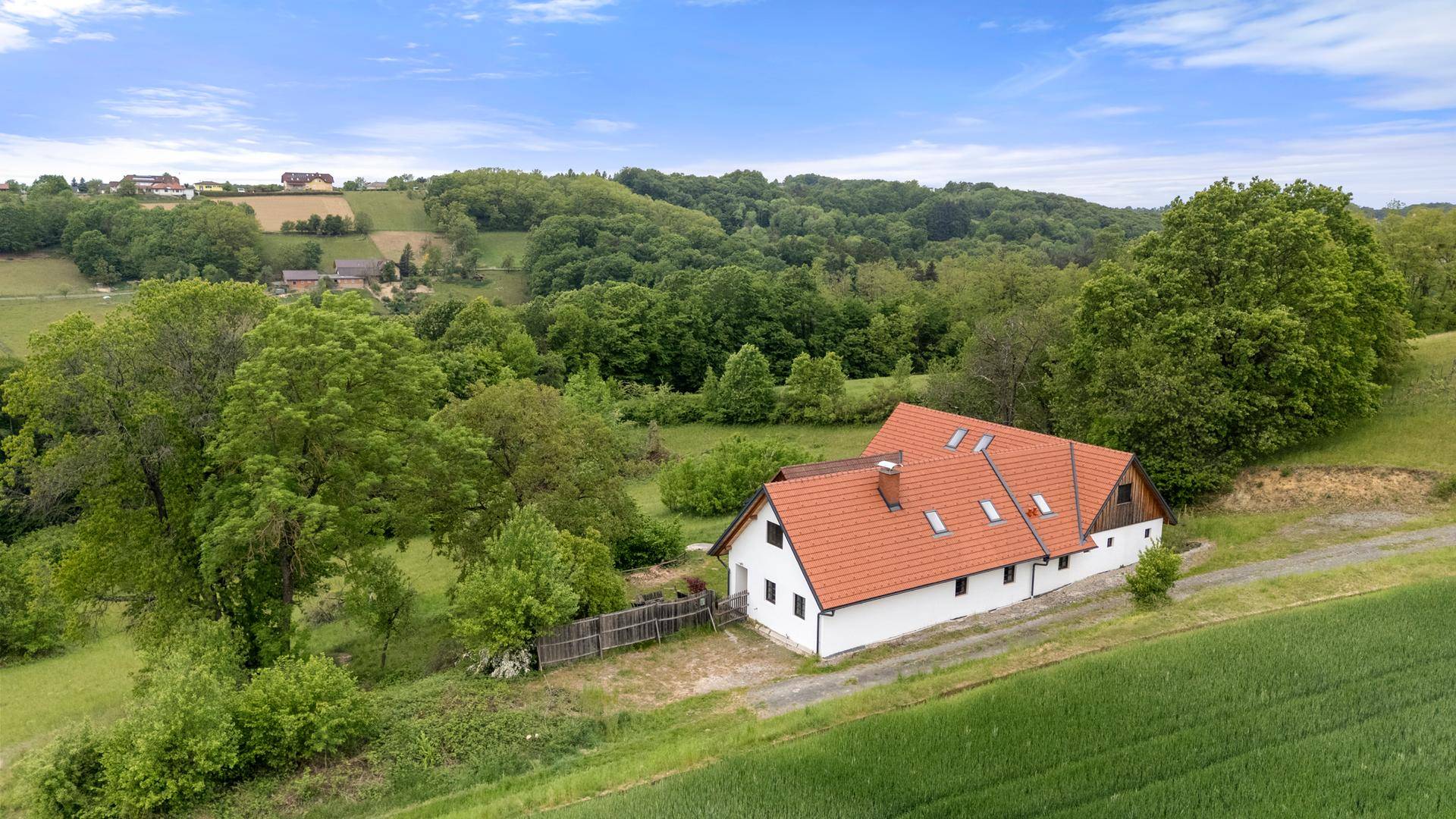 Luftaufnahme eines Landhauses mit rotem Ziegeldach, umgeben von grünen Hügeln und Feldern.
