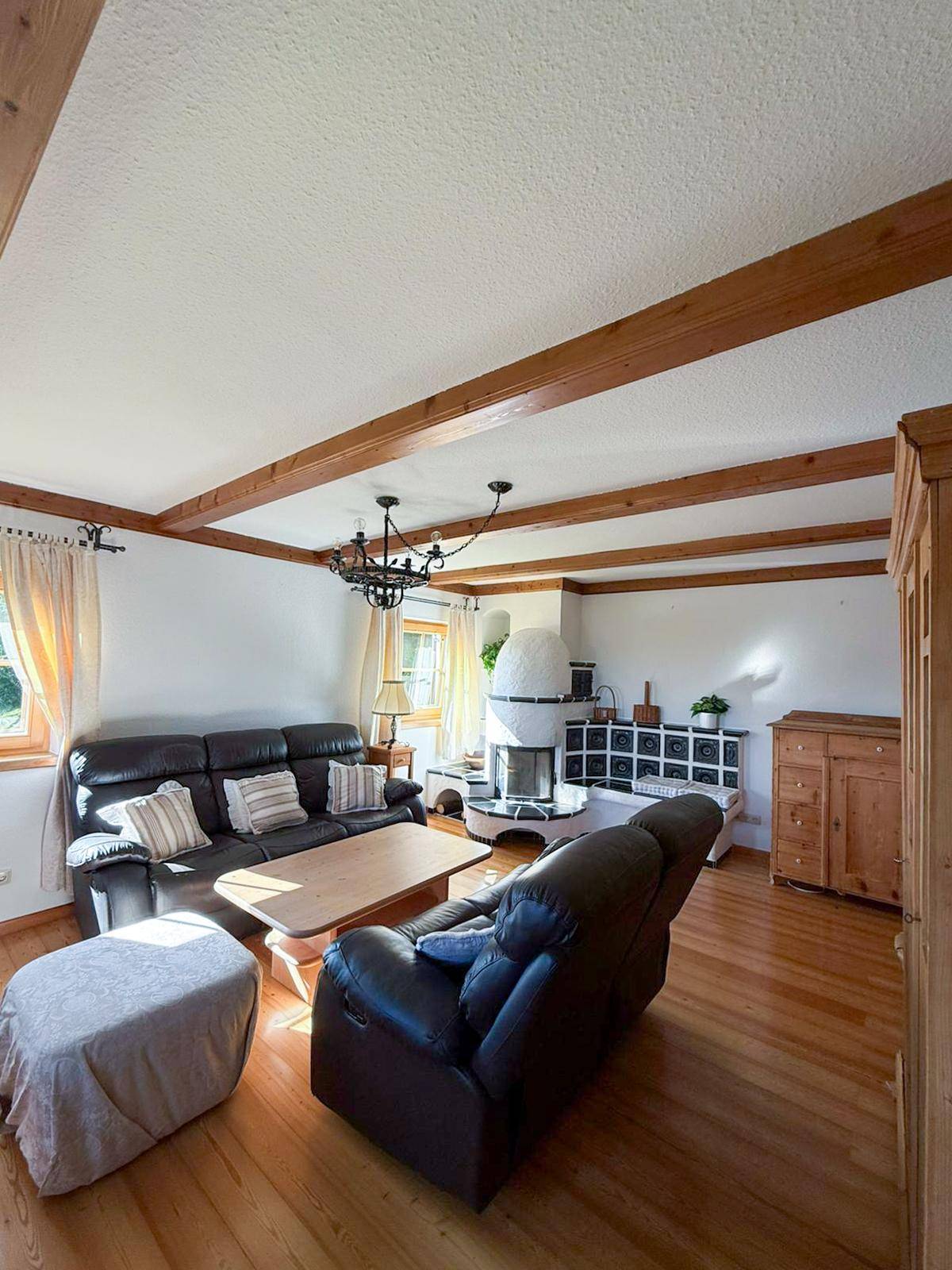 Gemütliches Wohnzimmer im Landhausstil mit Holzbalken, Parkettboden und einem traditionellen Kachelofen.