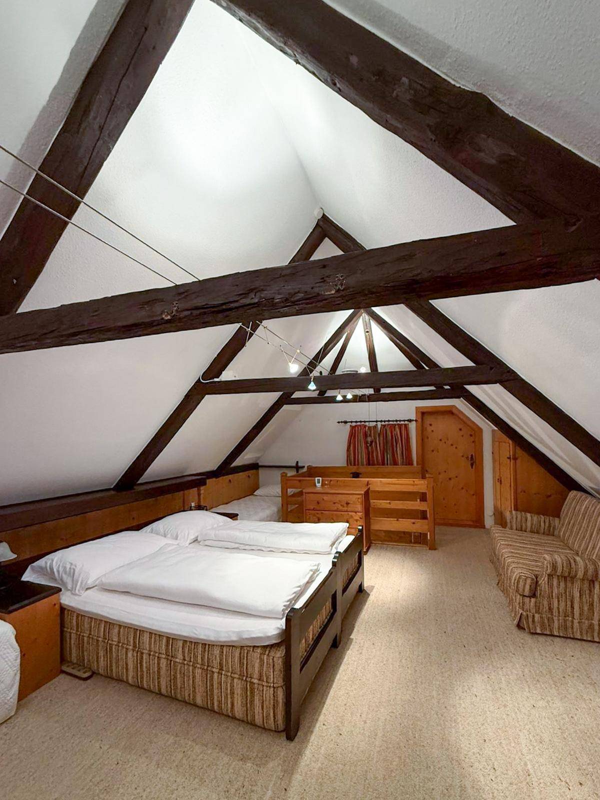 Schlafzimmer im Dachgeschoss mit sichtbaren Holzbalken, Dachschrägen und Teppichboden.
