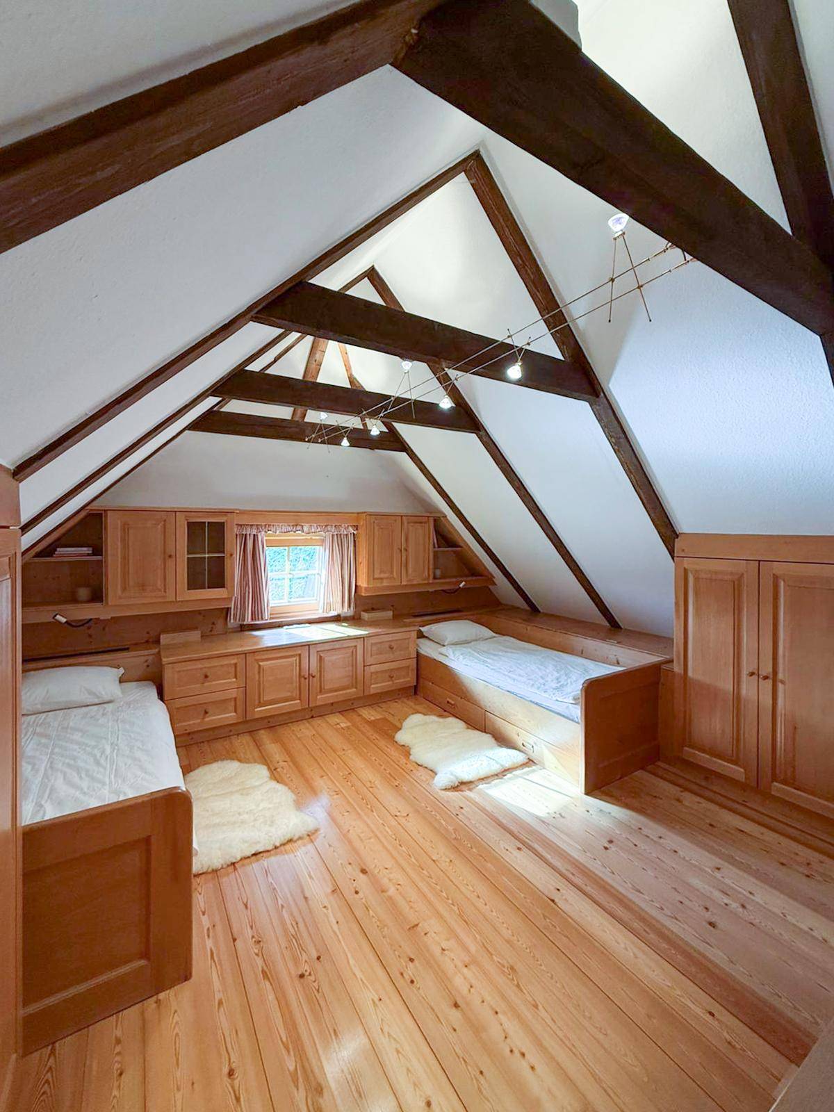 Helles Dachgeschoss-Schlafzimmer mit Holzboden, sichtbaren Balken und maßgefertigten Holzmöbeln.