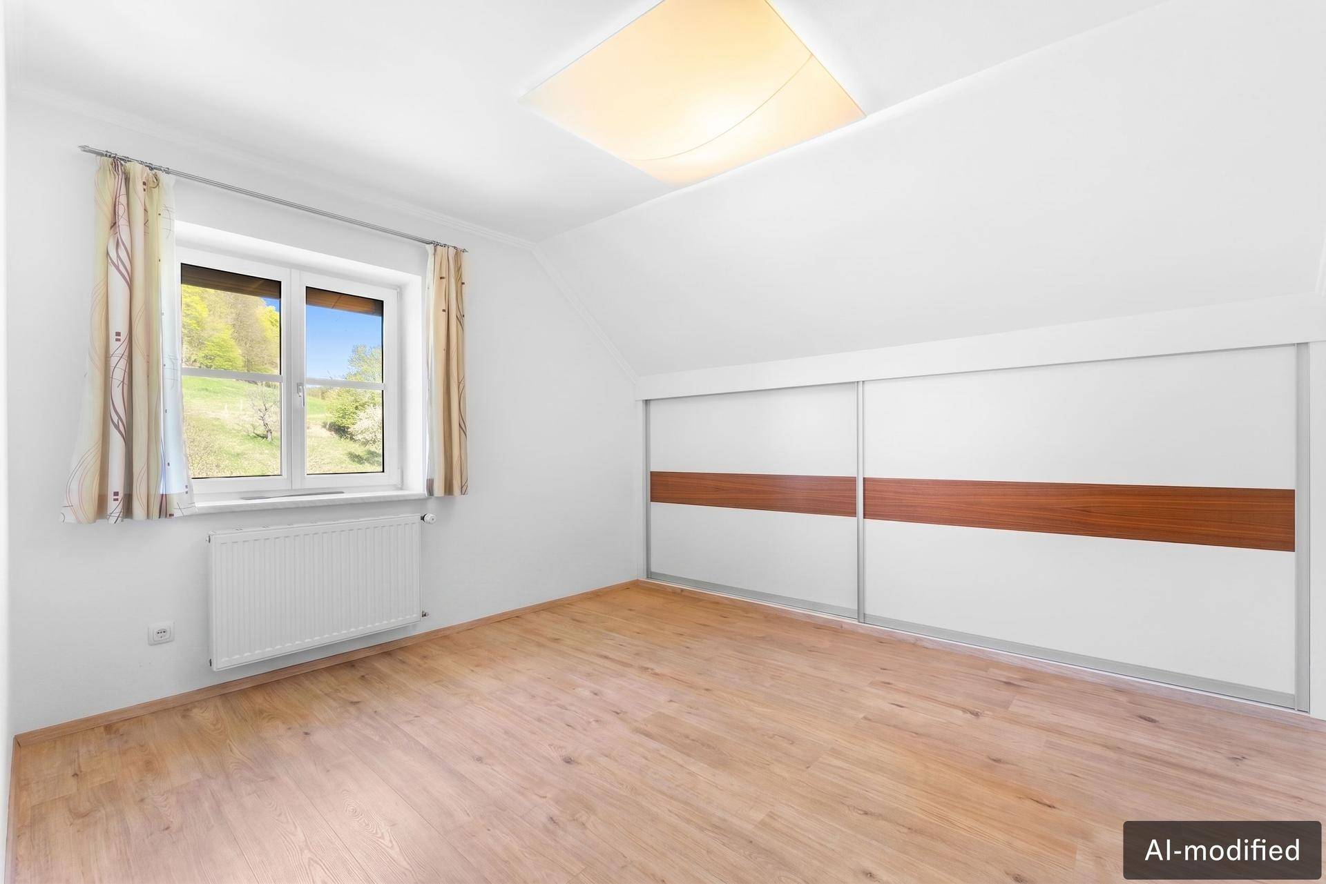Helles Schlafzimmer mit Holzboden, Einbauschrank und Fenster mit Blick auf die grüne Umgebung.