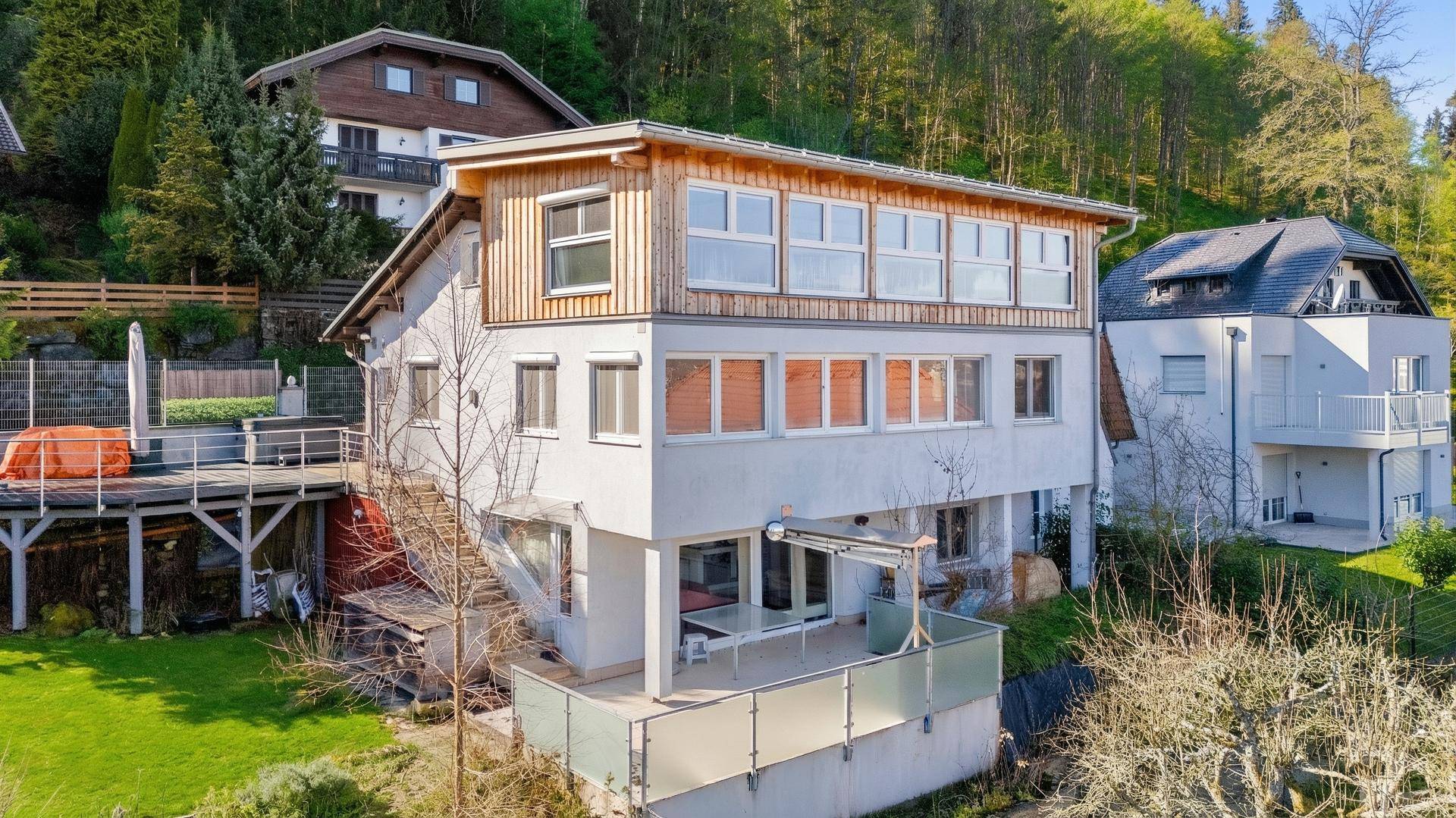 Mehrstöckiges Wohnhaus am Hang mit Terrassen und Blick auf die bewaldete Umgebung.