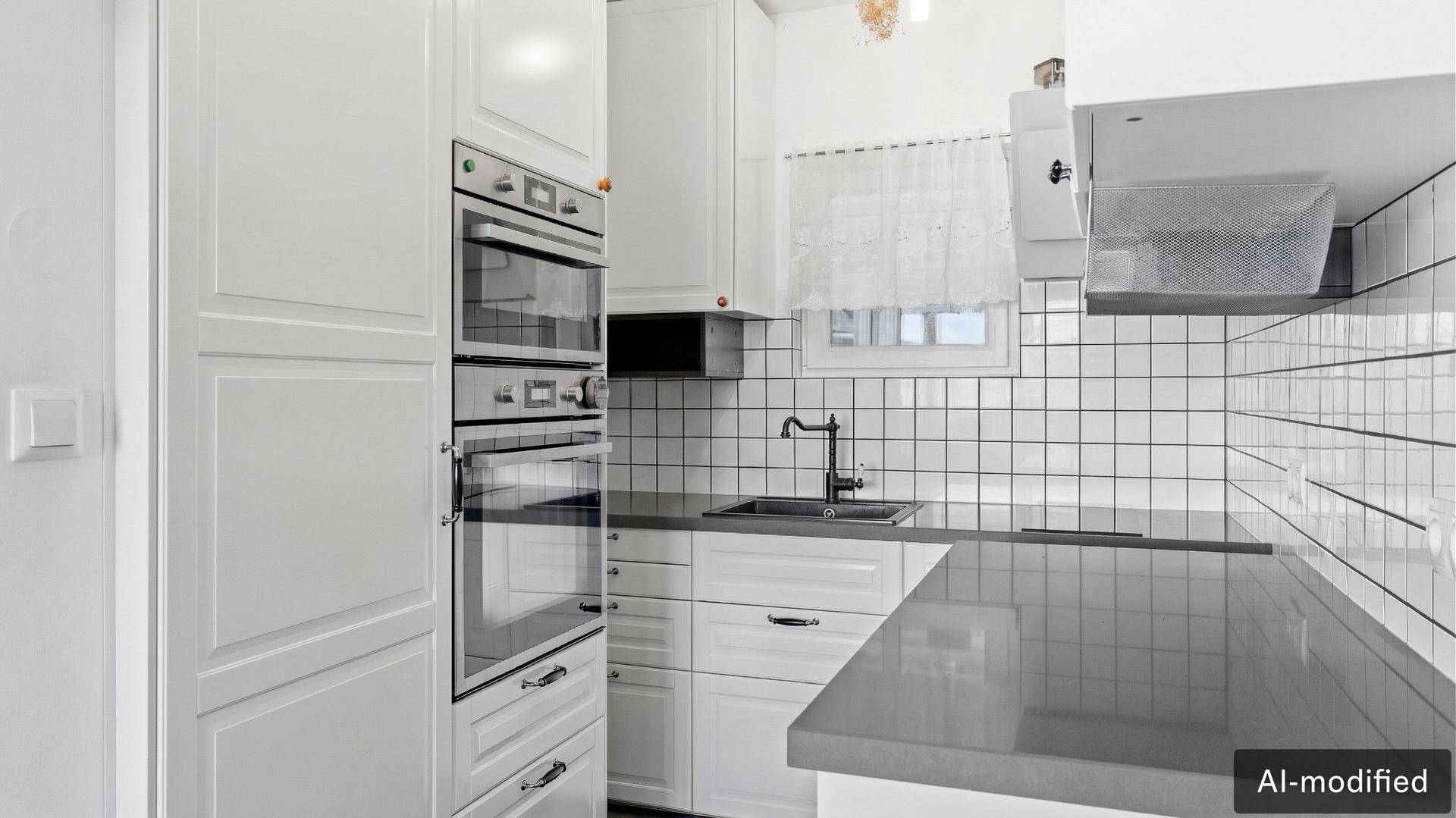 Moderne weiße Küche mit integrierten Backöfen, dunkler Arbeitsplatte und Fliesenrückwand.