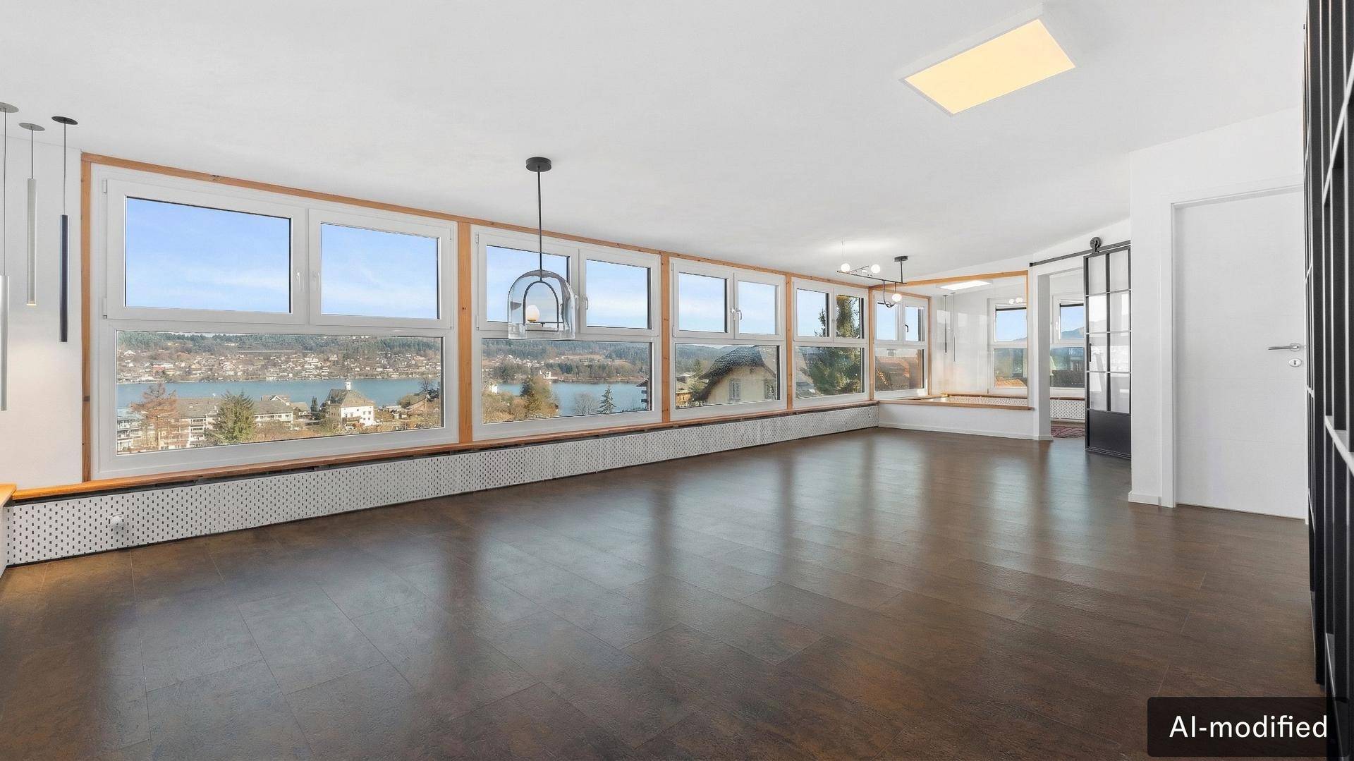 Geräumiges Wohnzimmer mit dunklem Holzboden und großen Fenstern mit Seeblick.
